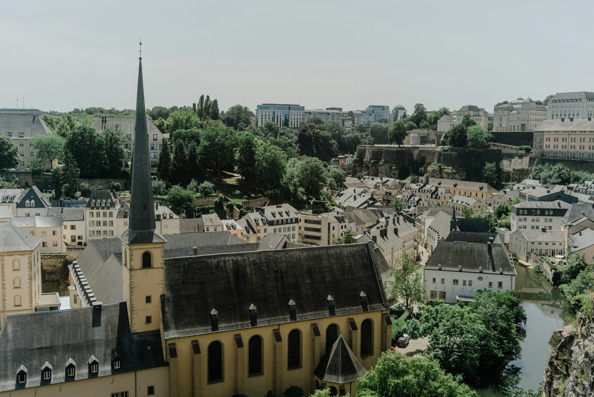 En vacker äldre kyrka i Luxemburg stad omgiven av byggnader och grönskande skog i bakgrunden under dagtid