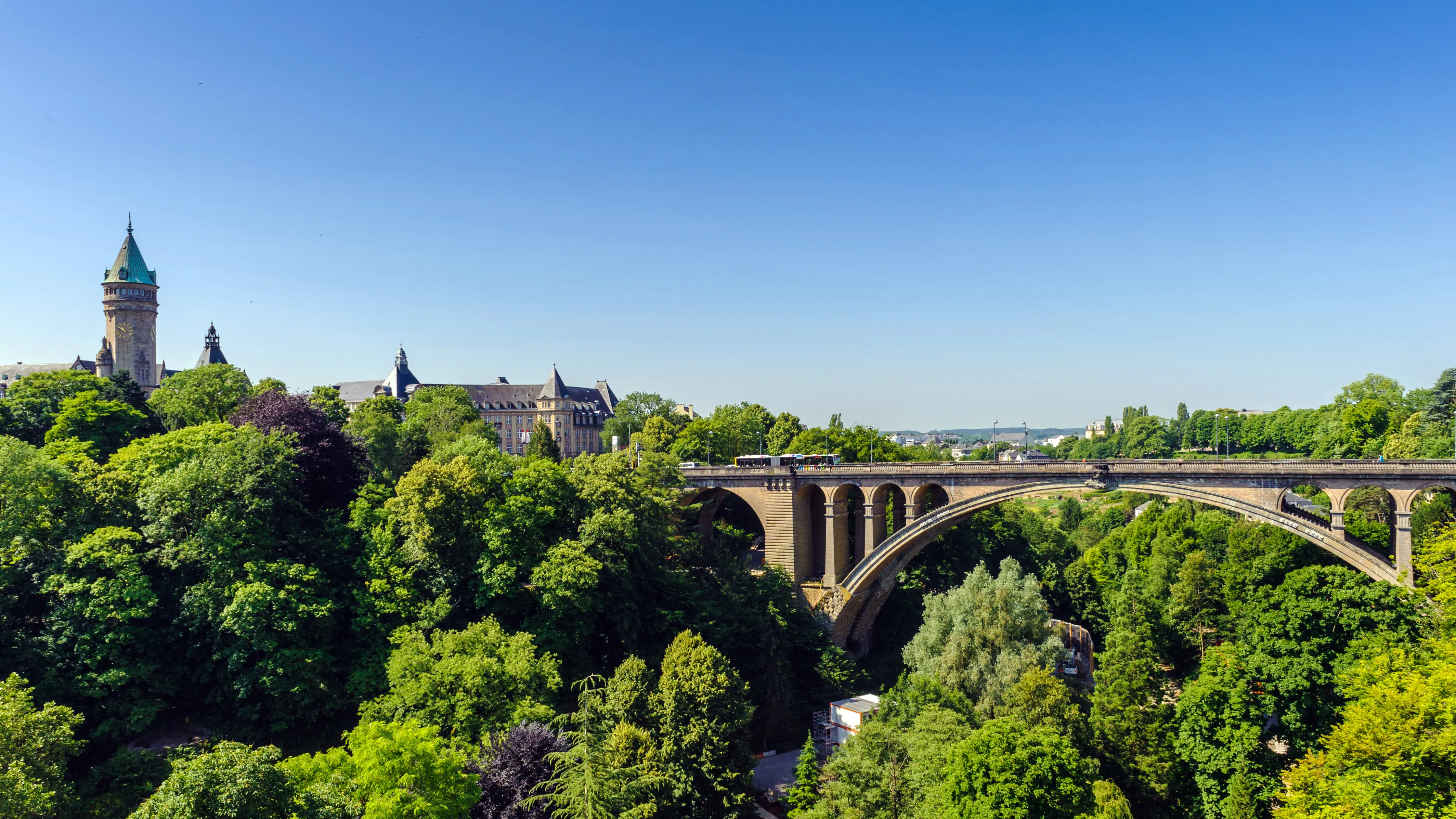 Resa till Luxemburg - Vy över Adolphe-bron i Luxemburg omgiven av grönska och med historiska byggnader i bakgrunden under en klarblå himmel.