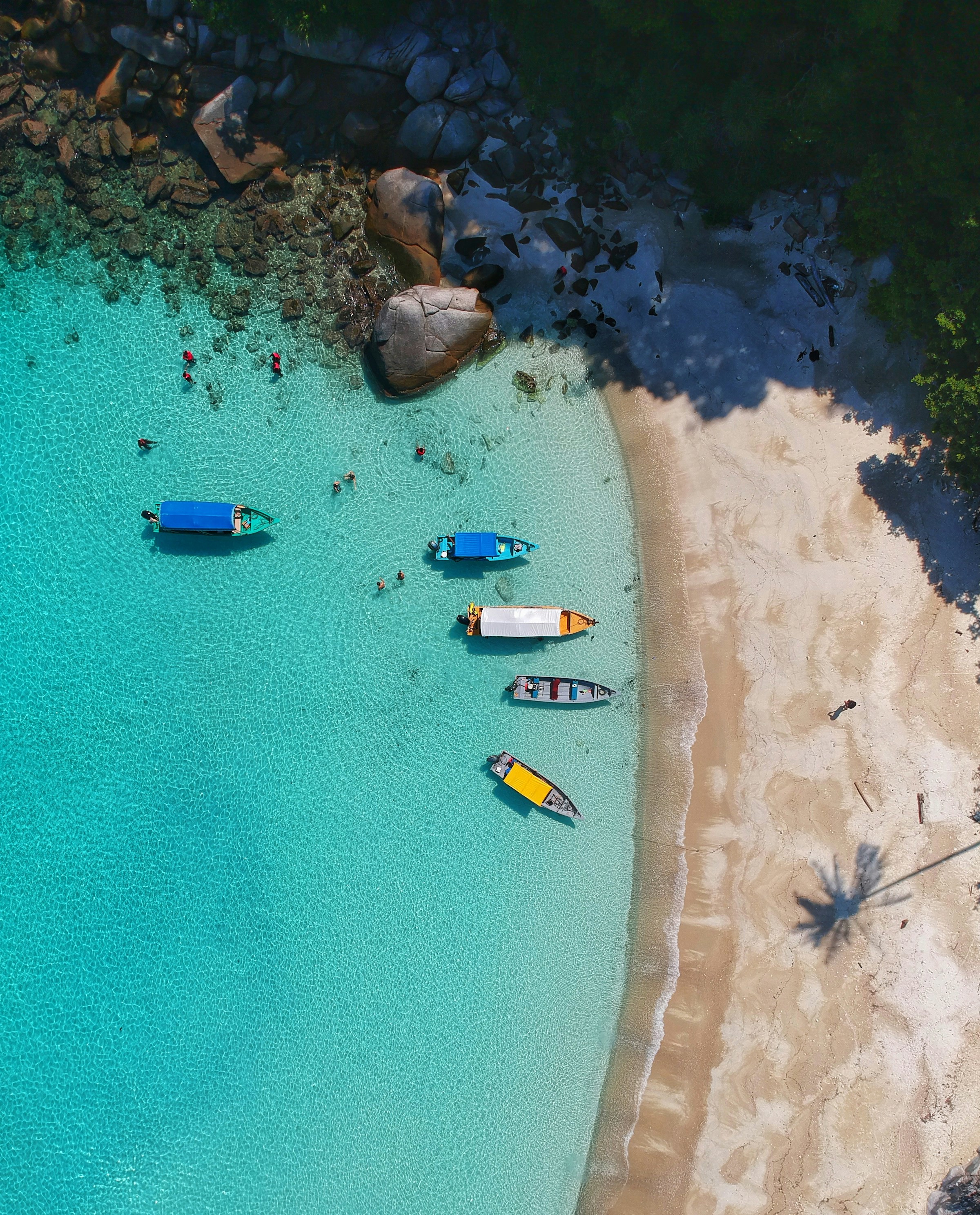 Vy ovanifrån på turkosblått vatten vid en strand med båtar och folk som badar i Malaysia