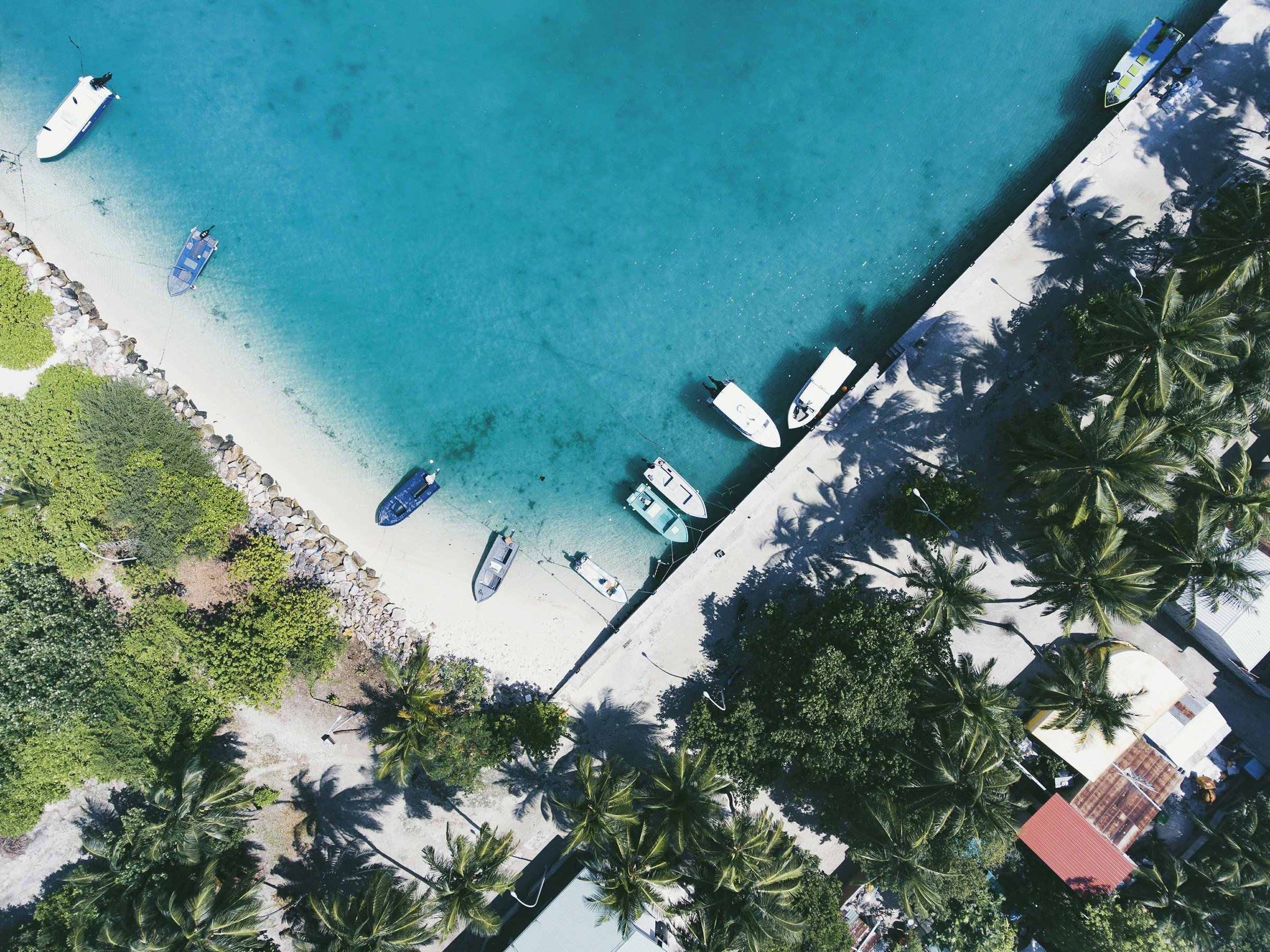 Flygfoto på en bukt och liten hamn i Maldiverna med ett hotell vid turkosblått vatten och båtar