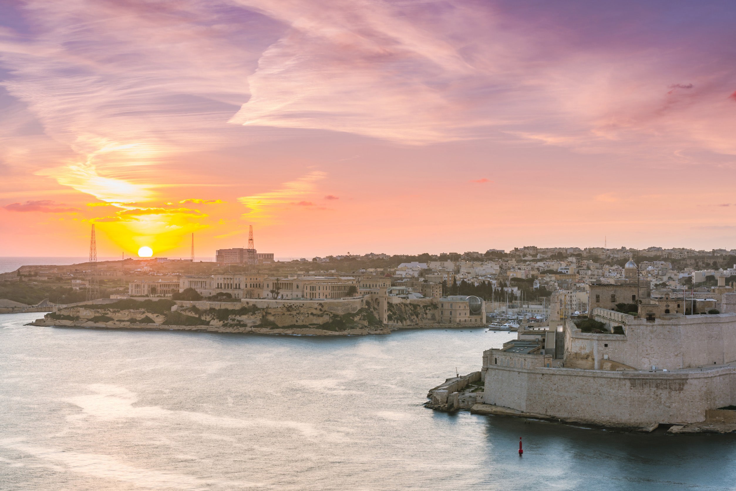 Solnedgång vid kusten av en stad på Malta med vackra byggnader och lugnt hav