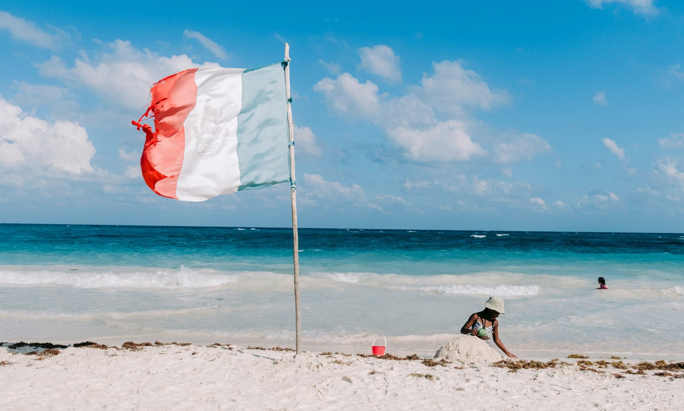 Strand med Mexikos flagga möts av blått hav i bakgrunden med folk som badar