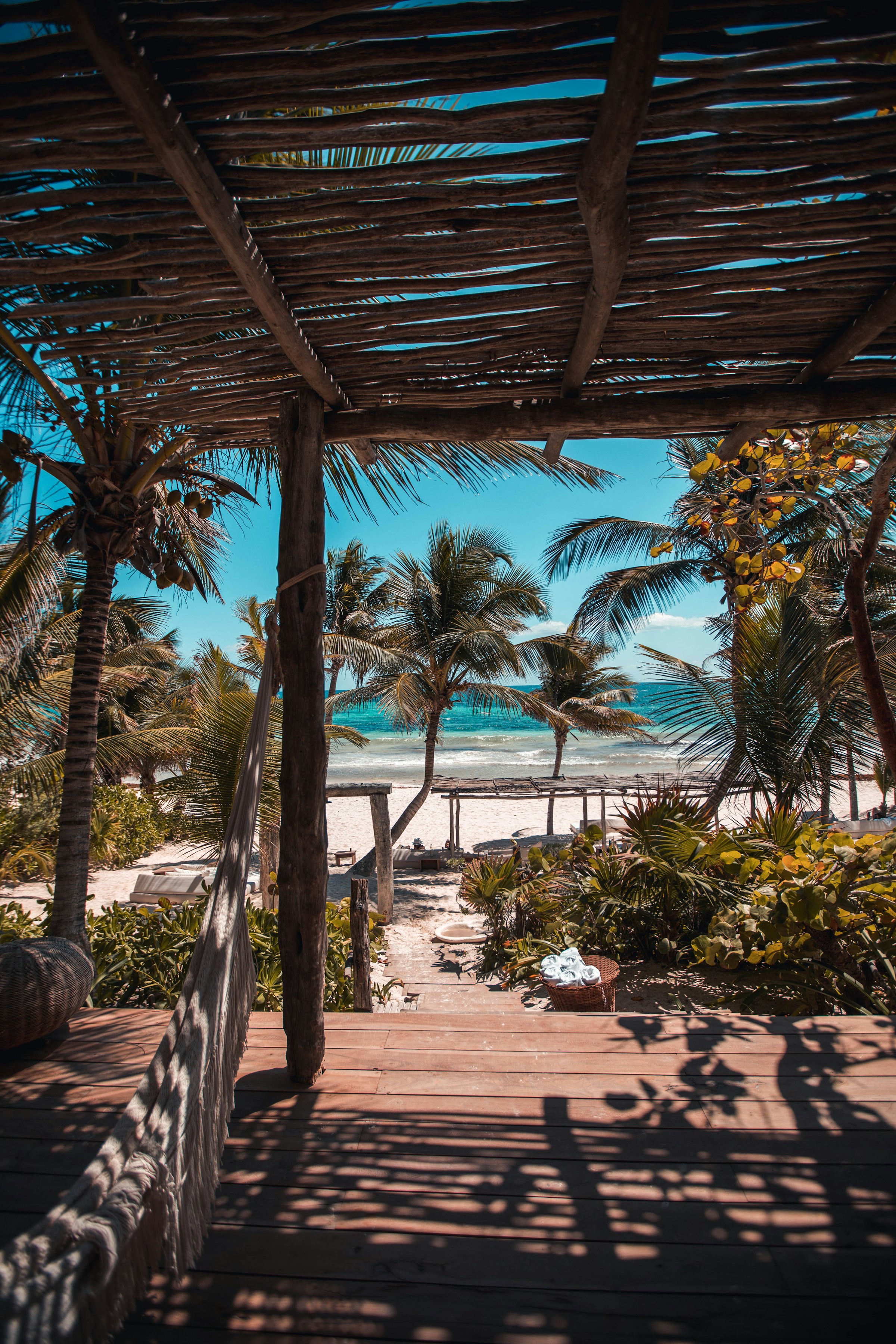 Gångväg från en taverna i Tulum, Mexico ut mot palmer och strand med blått hav i bakgrunden