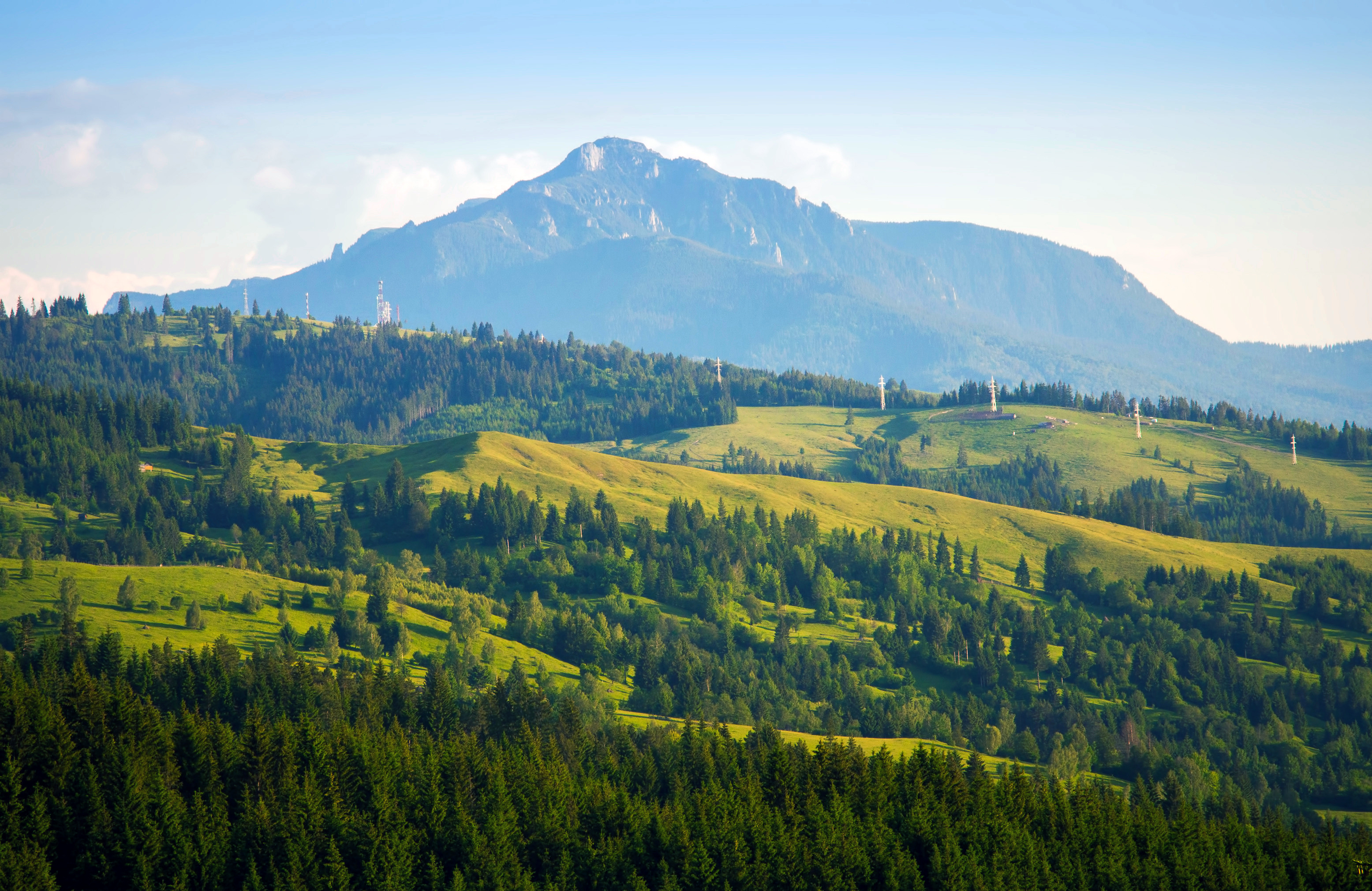 Resa till Moldavien - Frodig grön dal med skogstäckta kullar framför majestätiskt berg i solljus, naturskönt landskap.