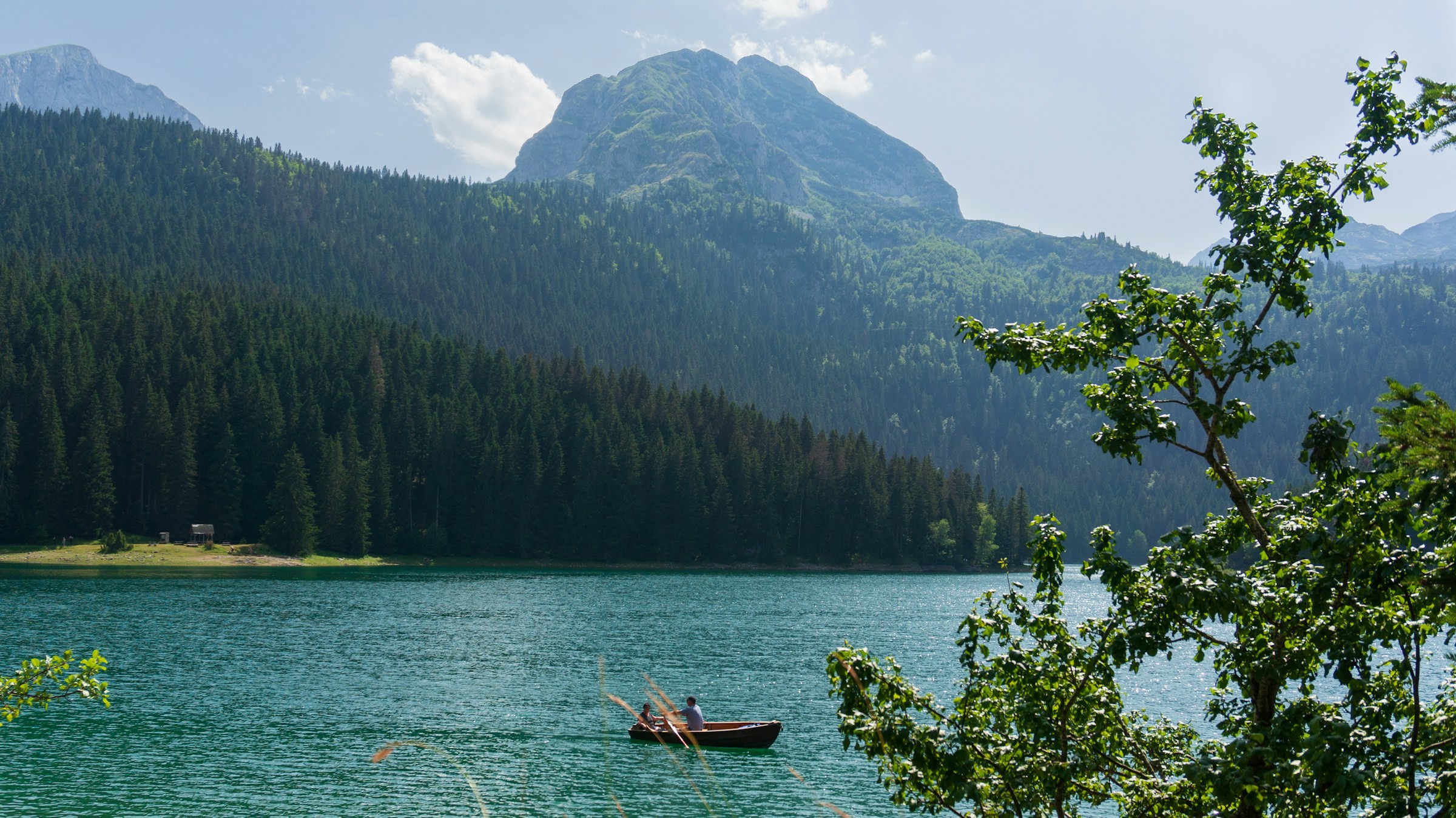 Vy över en sjö men en ensam roddbåt omringad av vacker natur och stora berg i bakgrunden i Montenegro