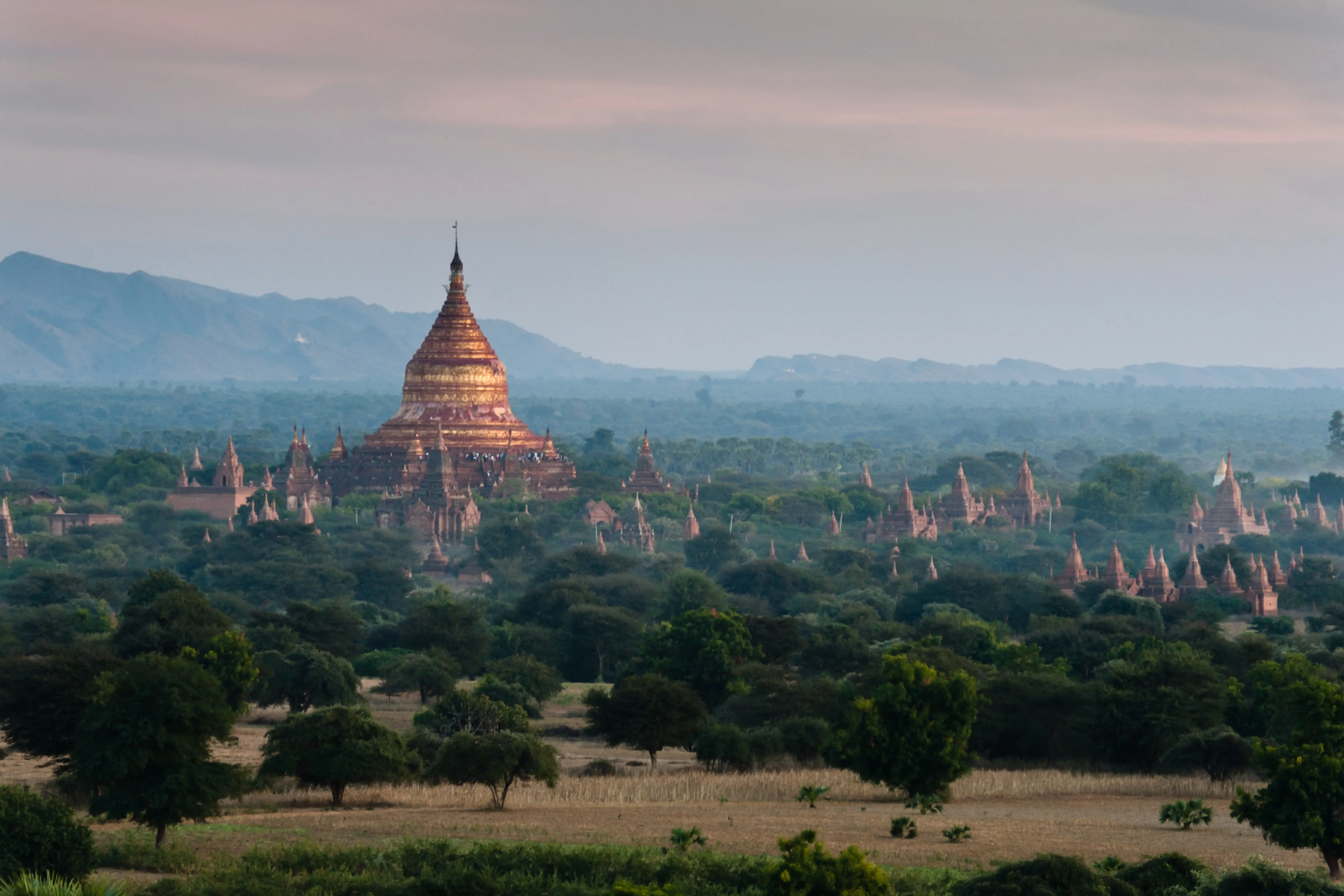 Resa till Myanmar - Vacker djungel kring ett asiatiskt tempel under en solnedgång med svag dimma och klippor i bakgrunden