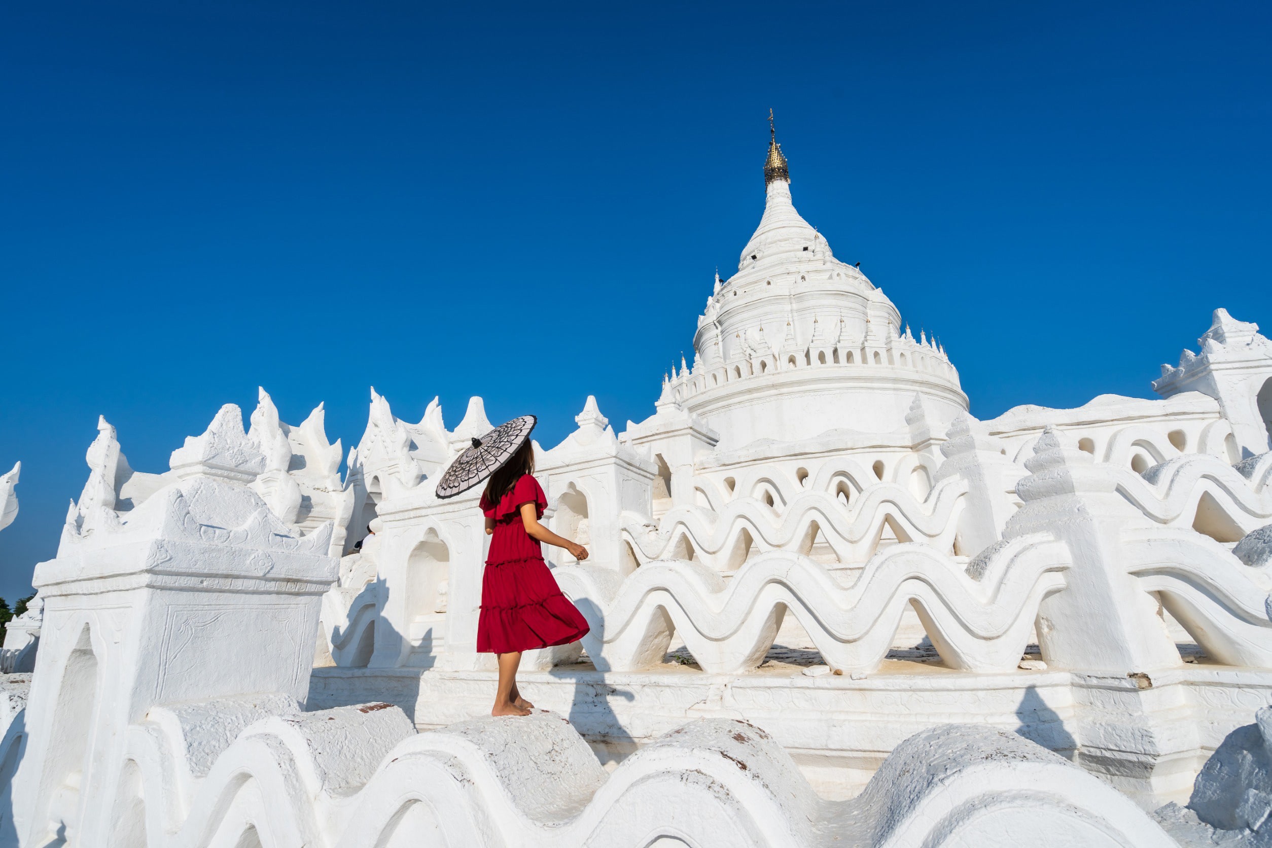 Beautiful white temple with a woman in red dress facing away with clear blue sky in the background