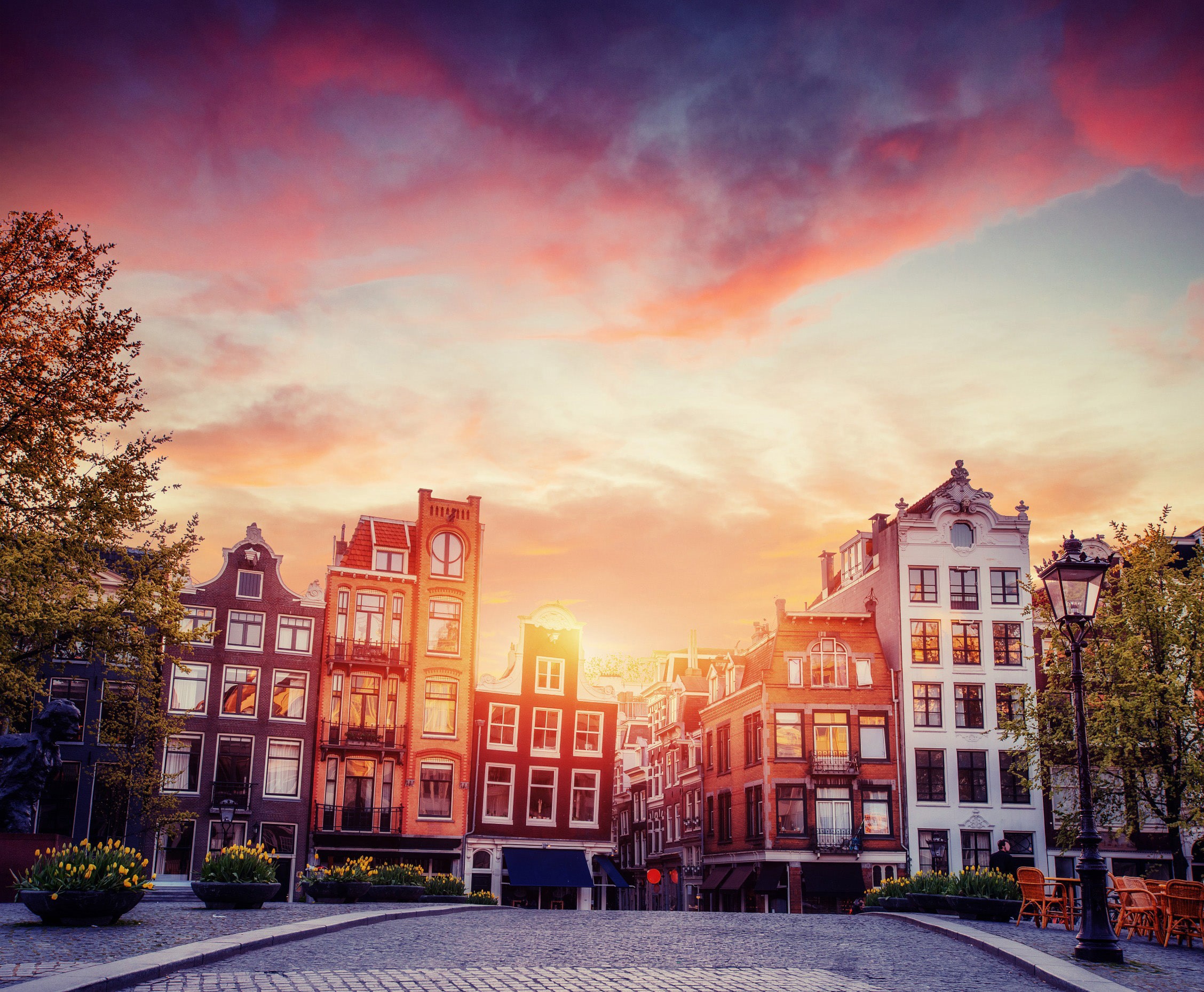 Solnedgång mellan byggnader vid ett torg i Amsterdam i Nederländerna. 