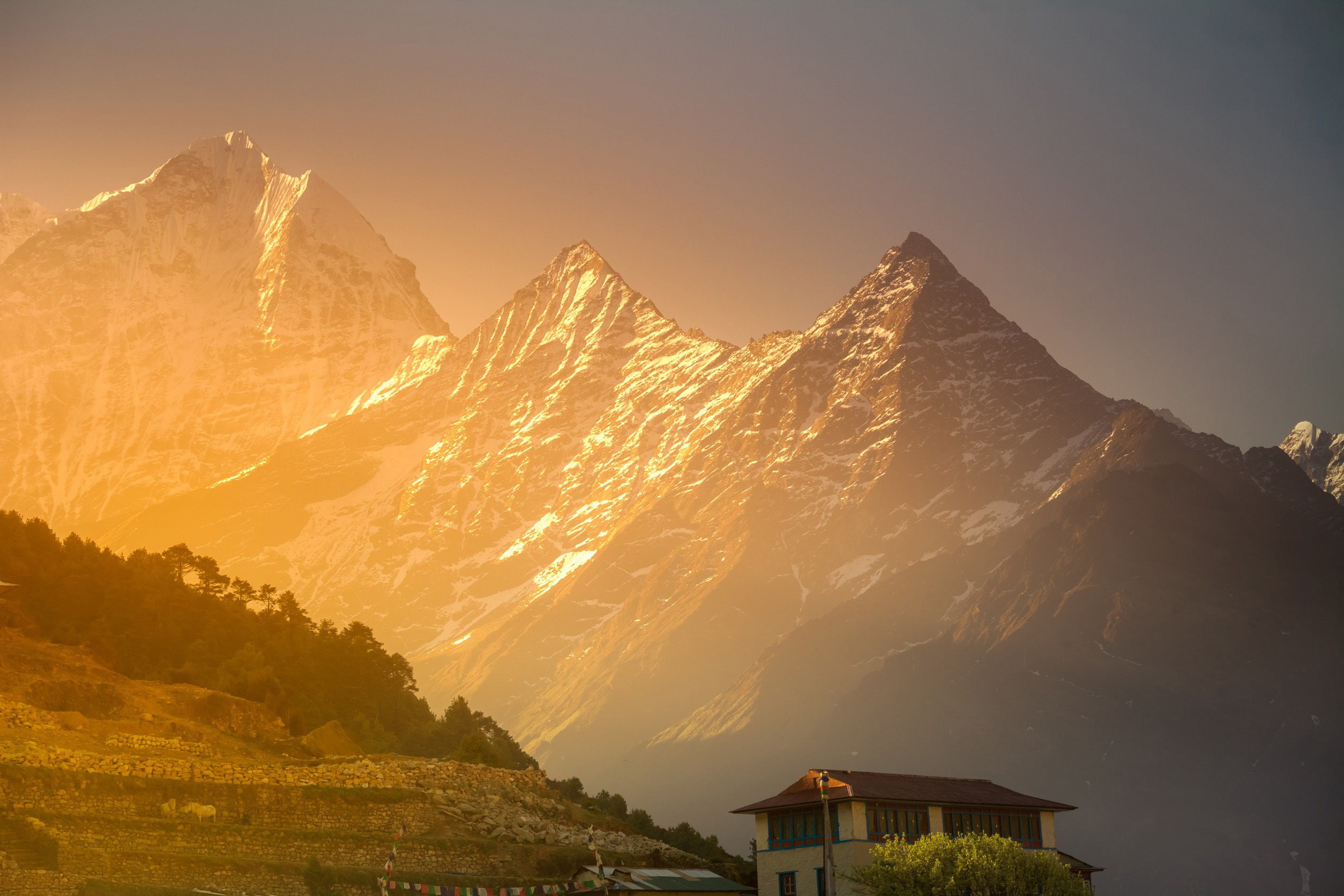 Solnedgång över Himalaya bergen i Nepal med ett hus i änden av en sluttning