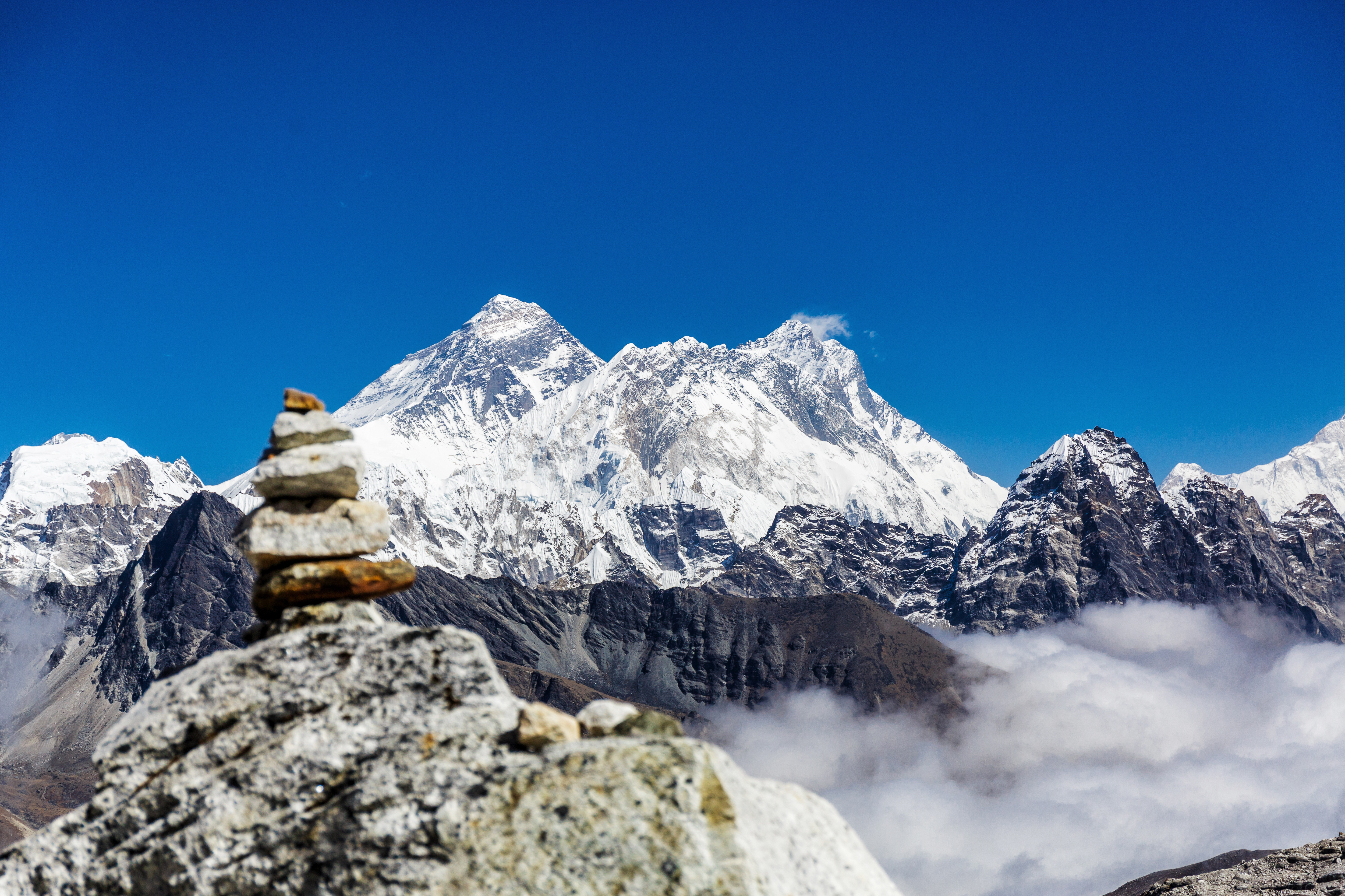 Resa till Nepal - Stenstapel i förgrunden med Mount Everest och Himalayabergen i bakgrunden över molnen under en klar himmel.