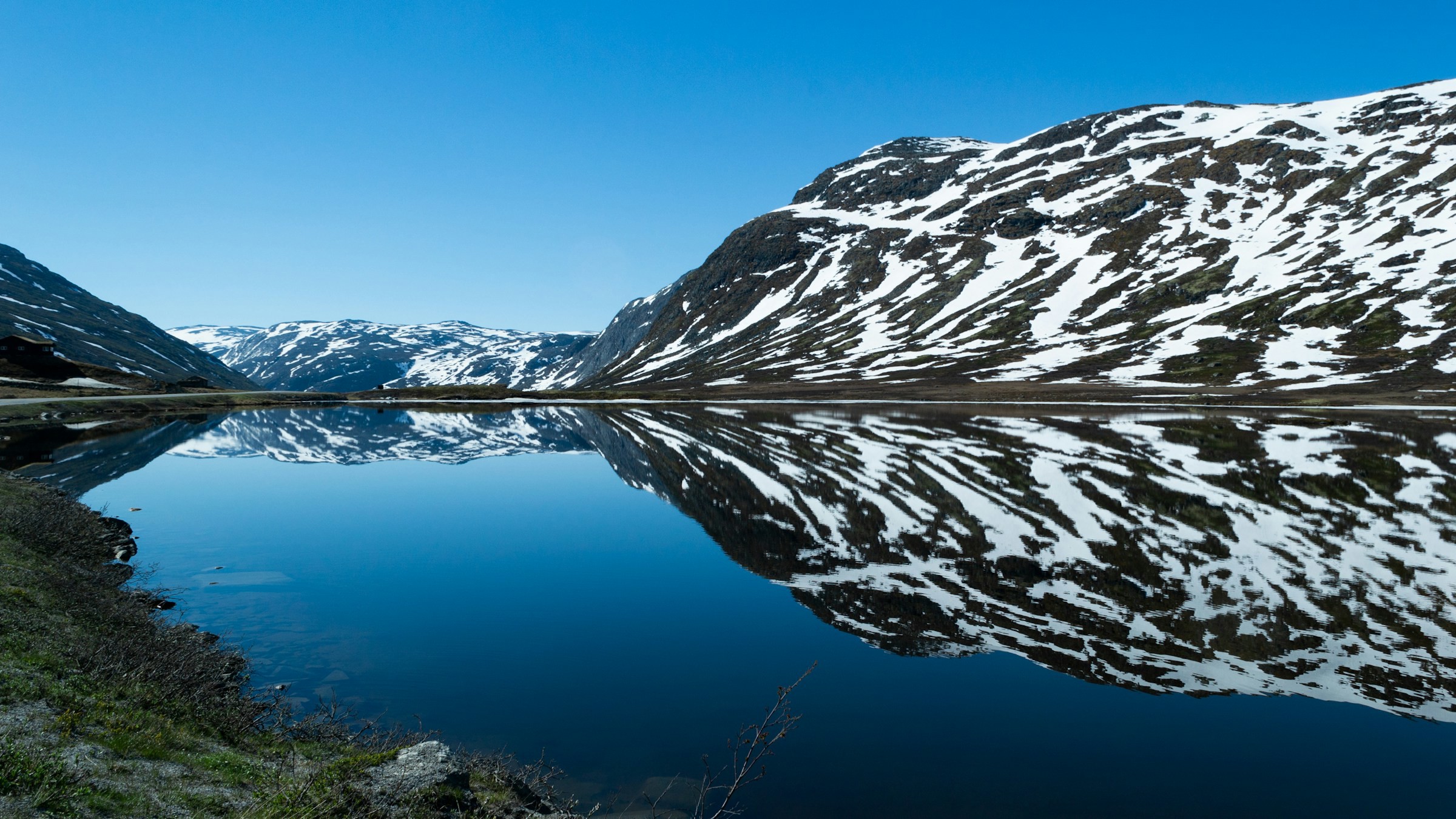 Stillsam sjö som leder upp mot norska fjorden i Hemsedal med blå himmel i bakgrunden