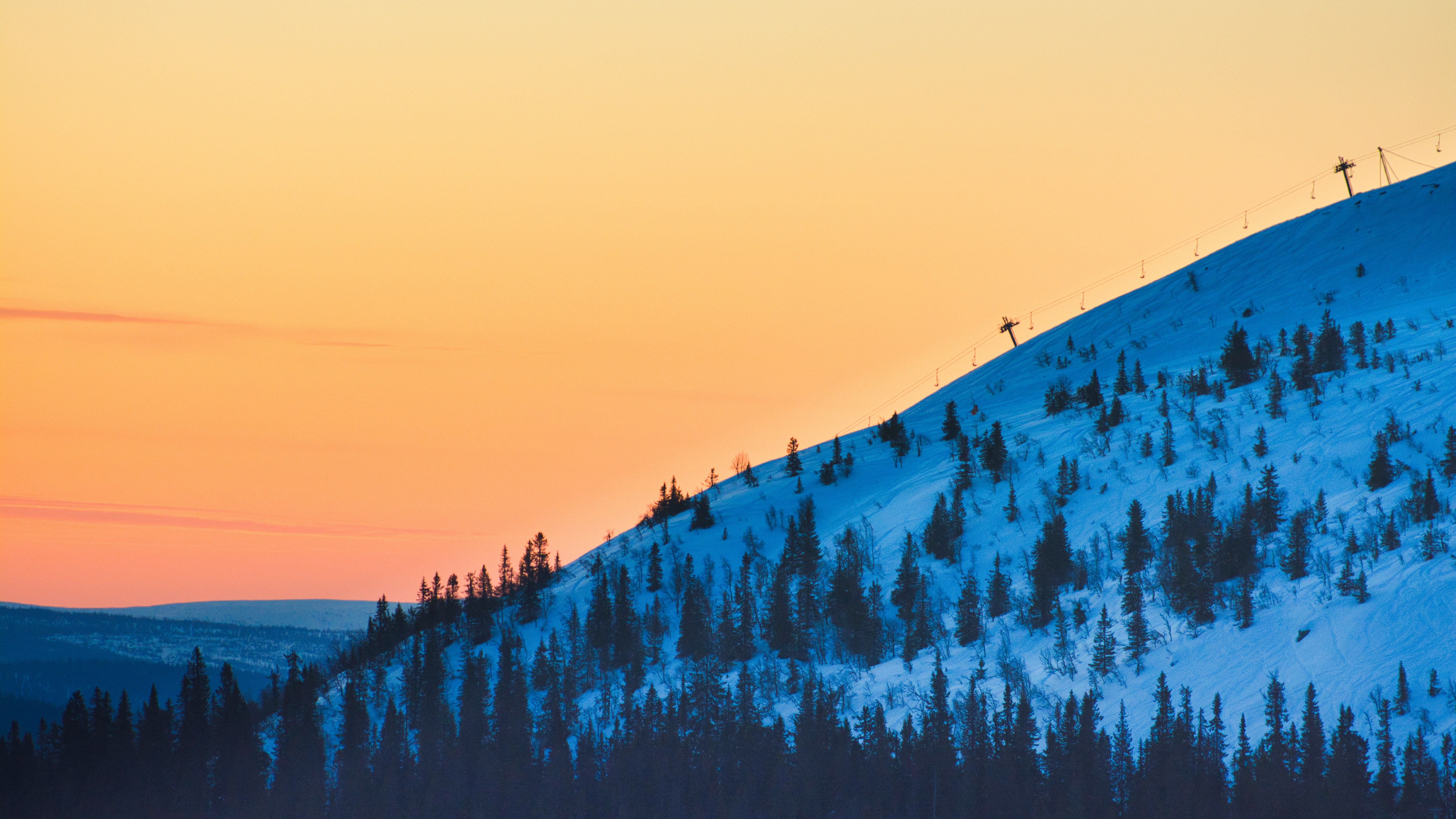 Resa till Trysil - Solnedgång över en snötäckt skidbacke i Trysil med en orange himmel i bakgrunden