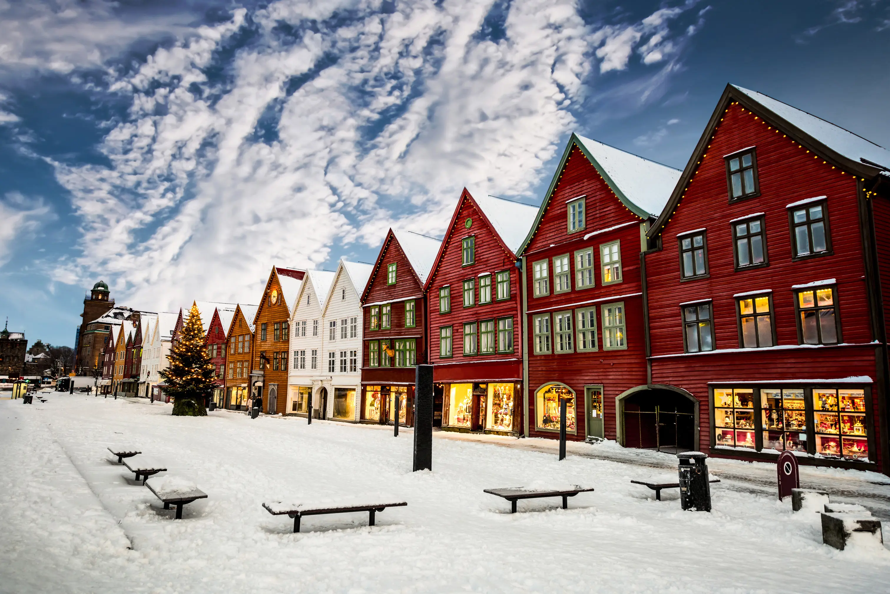 Resa till Bergen - Snötäckt gata med färgglada, historiska trähus på Bryggen i Bergen, Norge, under en klar vinterdag med blå himmel och dramatiska moln.