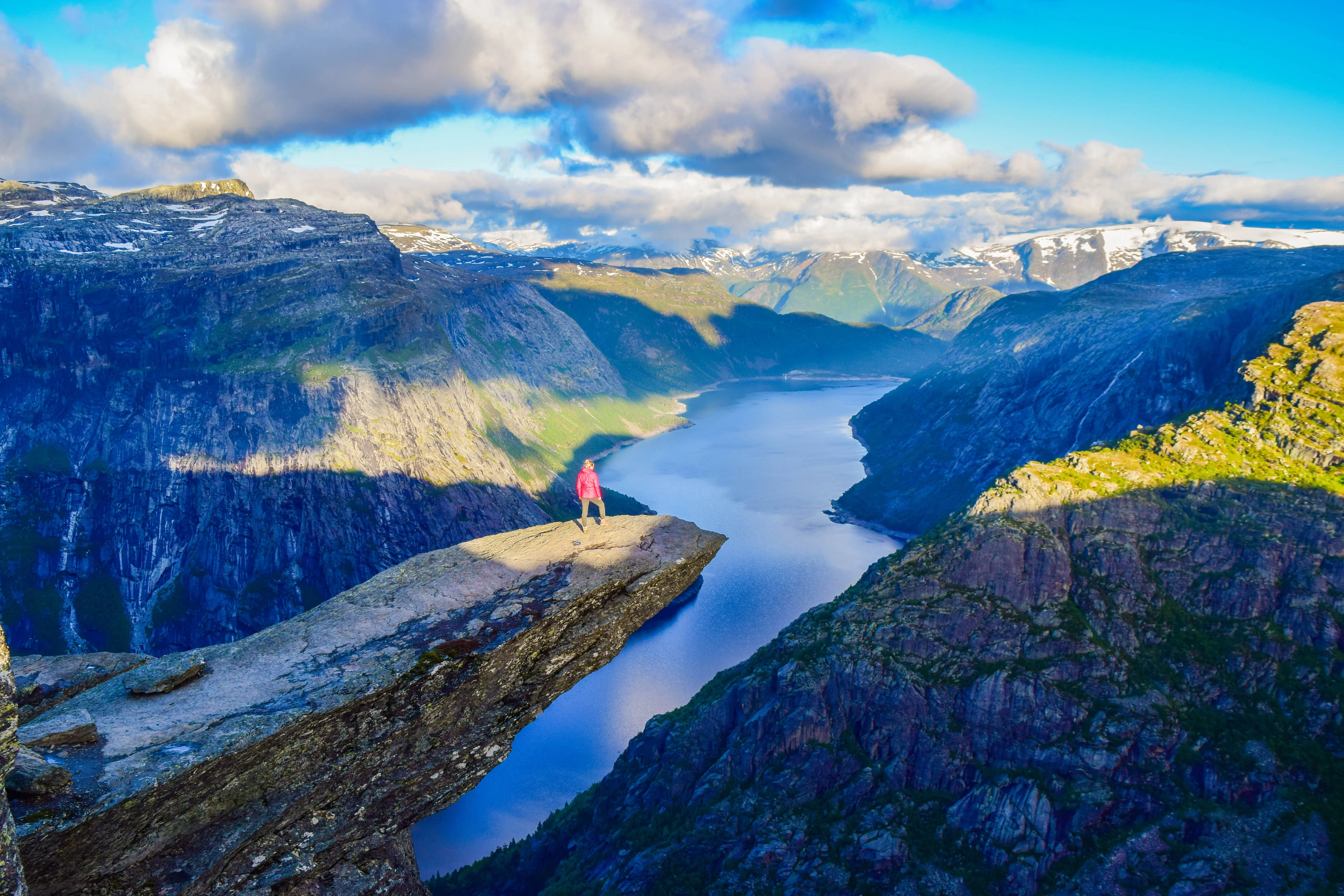 Resa till Norge - Person i röd jacka står på Trolltunga med utsikt över fjord och berg i Norge.