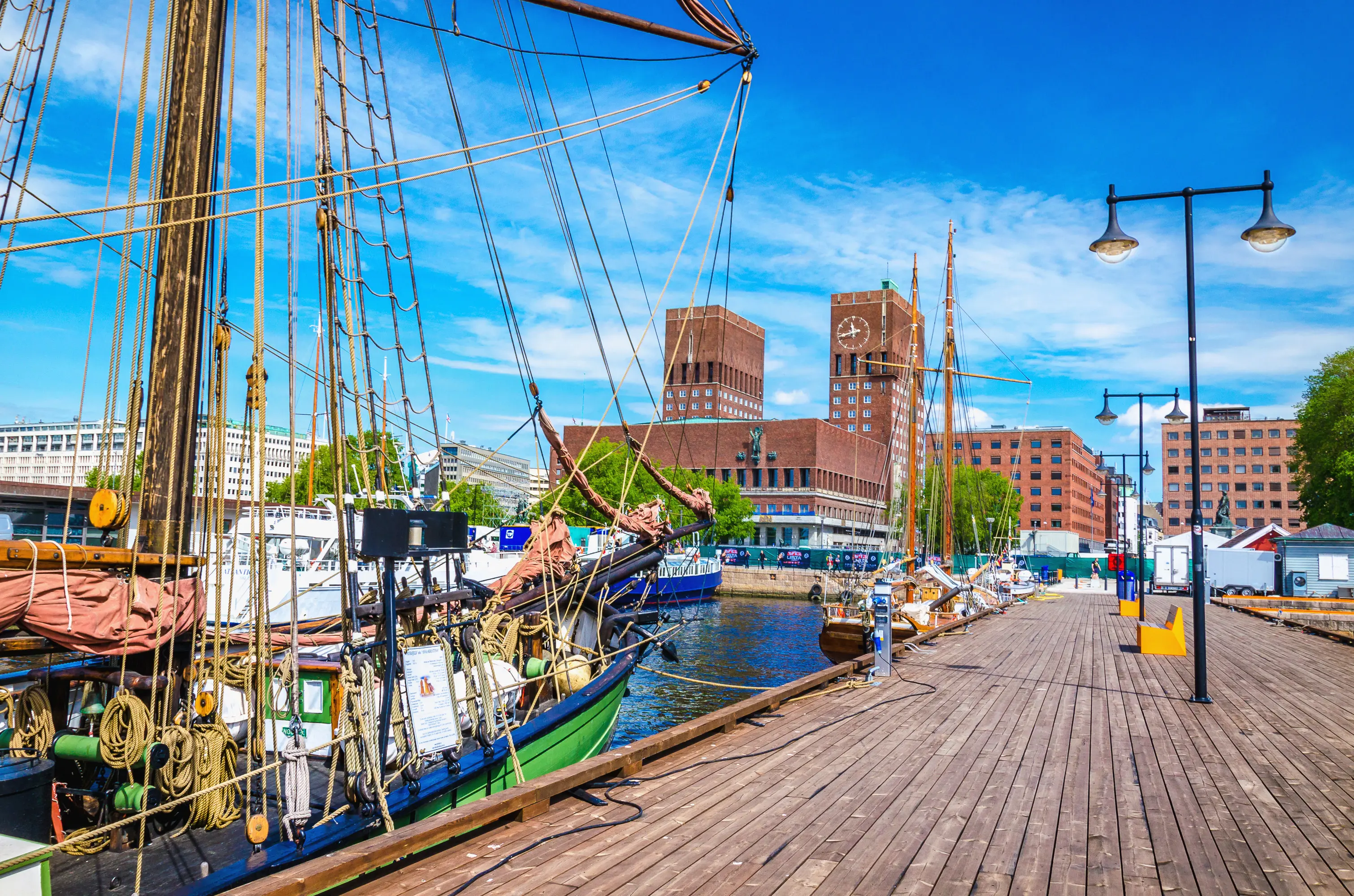 Resa till Oslo - Livlig marina med klassiska segelfartyg förtöjda vid kajen på en solig dag, med moderna byggnader i bakgrunden.