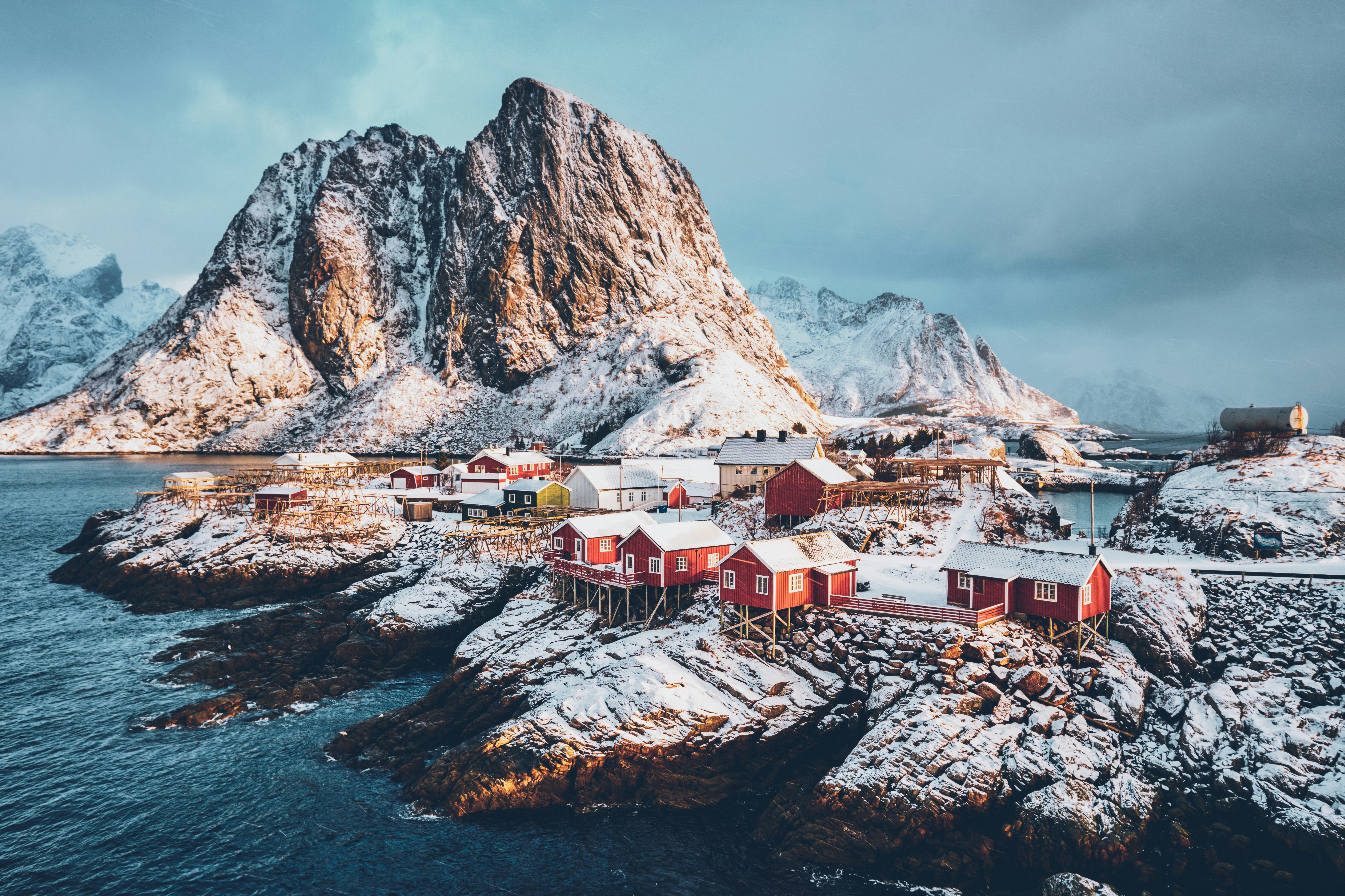 Vackra snötäckta berg möter havet vid Norska kusten med en en himmel fylld av moln i bakgrunden