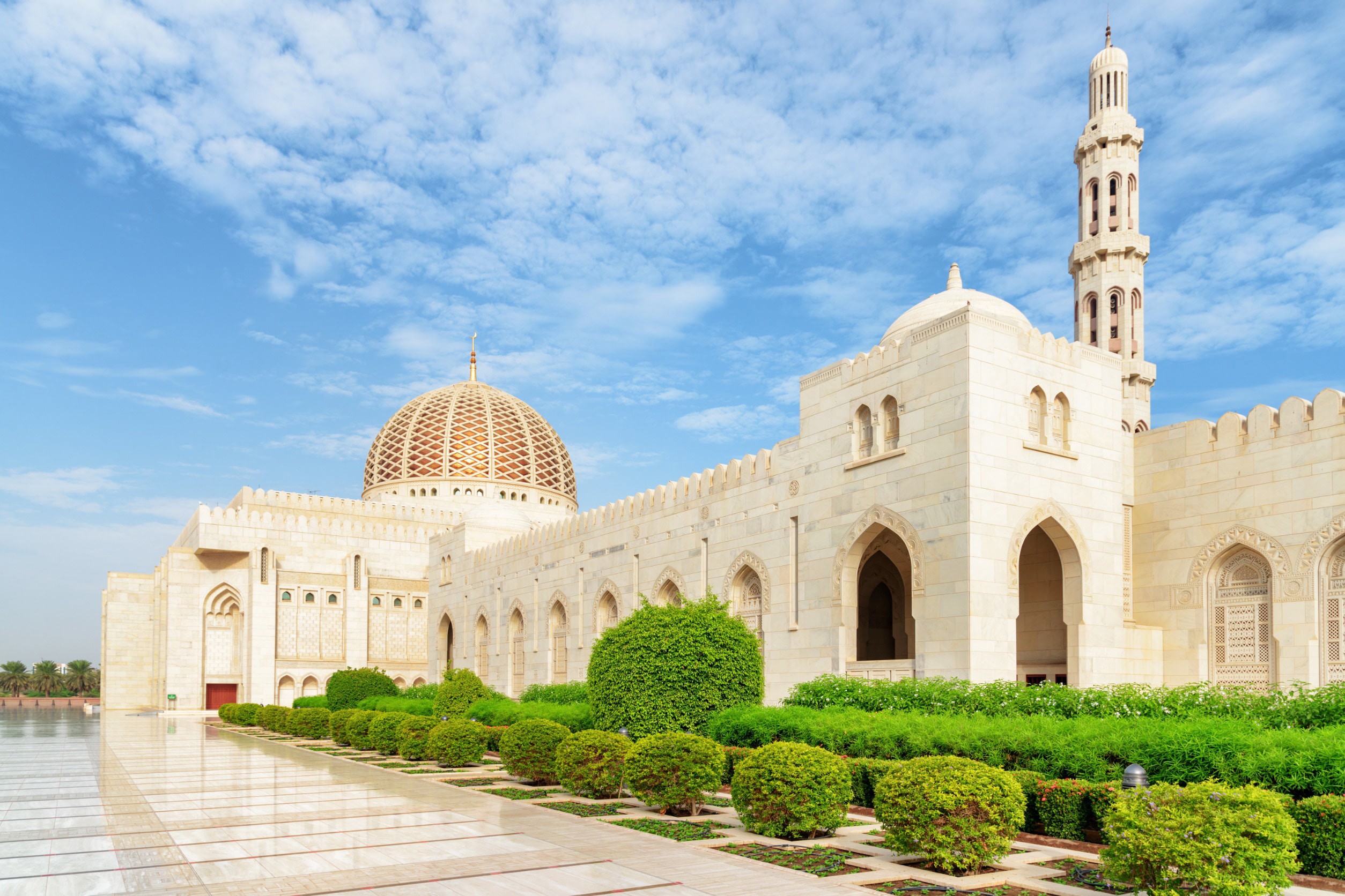 Beautiful White Mosque in Muscat with Green Bushes Around And Clear Blue Sky in the Background