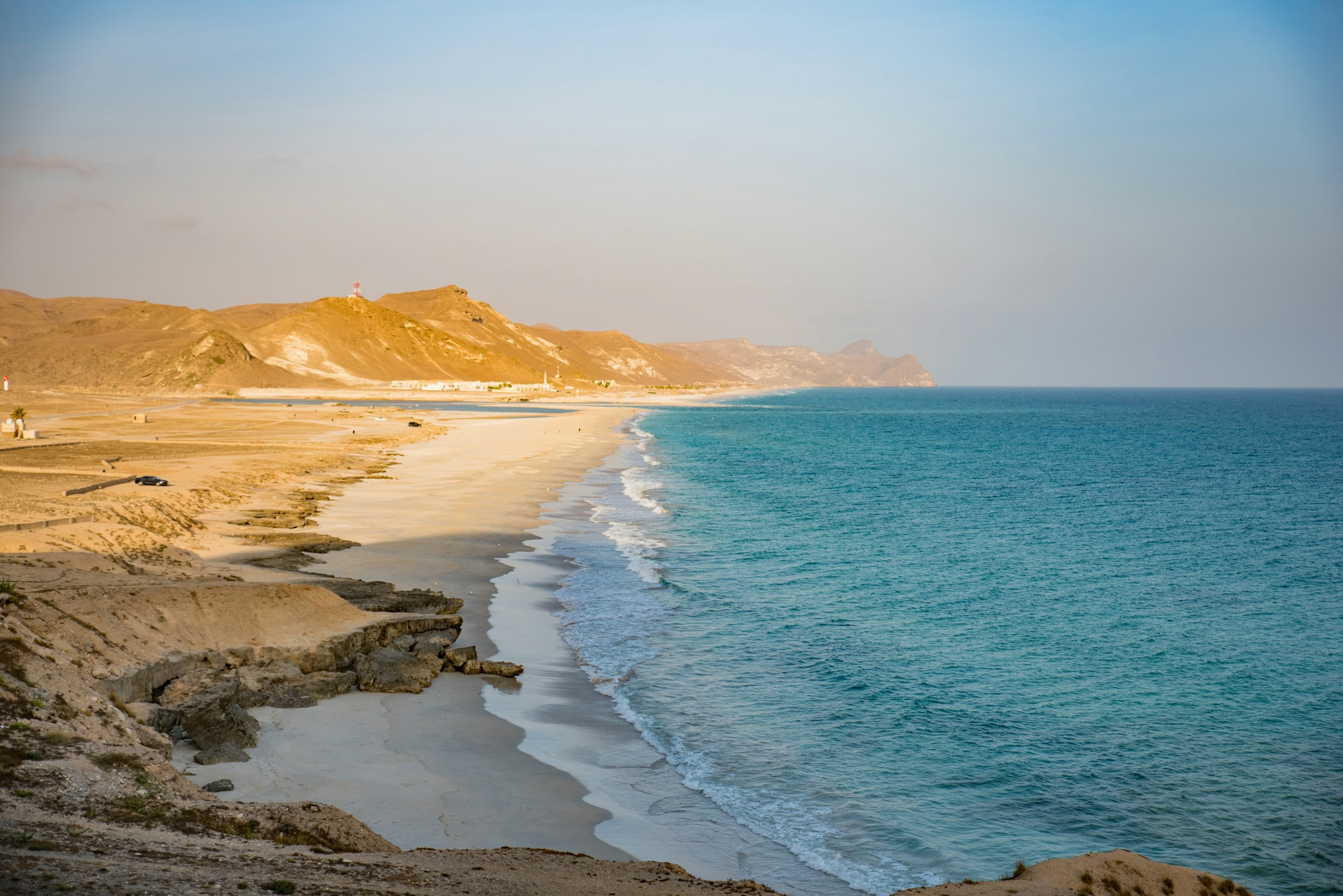 Vy över kusten av Oman där blått hav möter en lång kust och sandig strand med vågor ut till horisonten