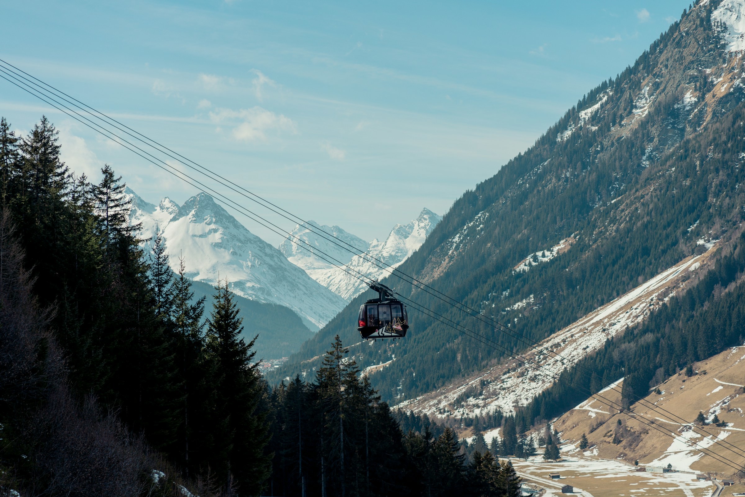 Bergbana över alpin dal med snötäckta bergstoppar och tallskog i förgrunden i Ischgl.