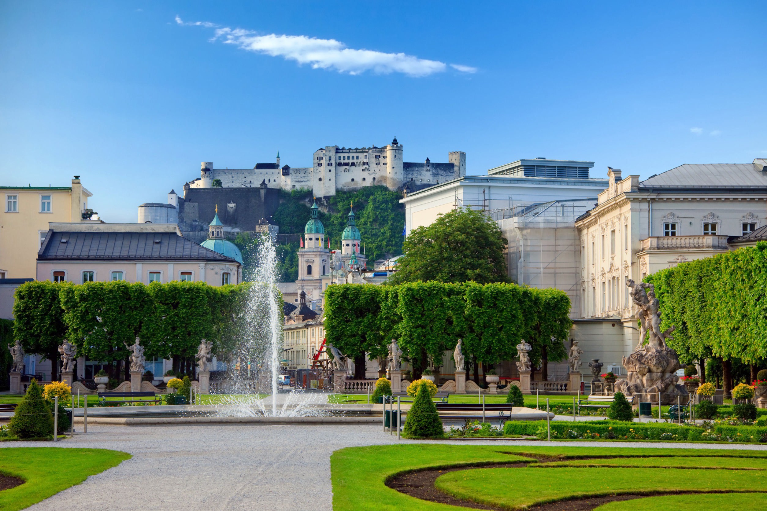 Vacker grön park med traditionella europeiska byggnader och fontän mot en blå himmel i Salzburg