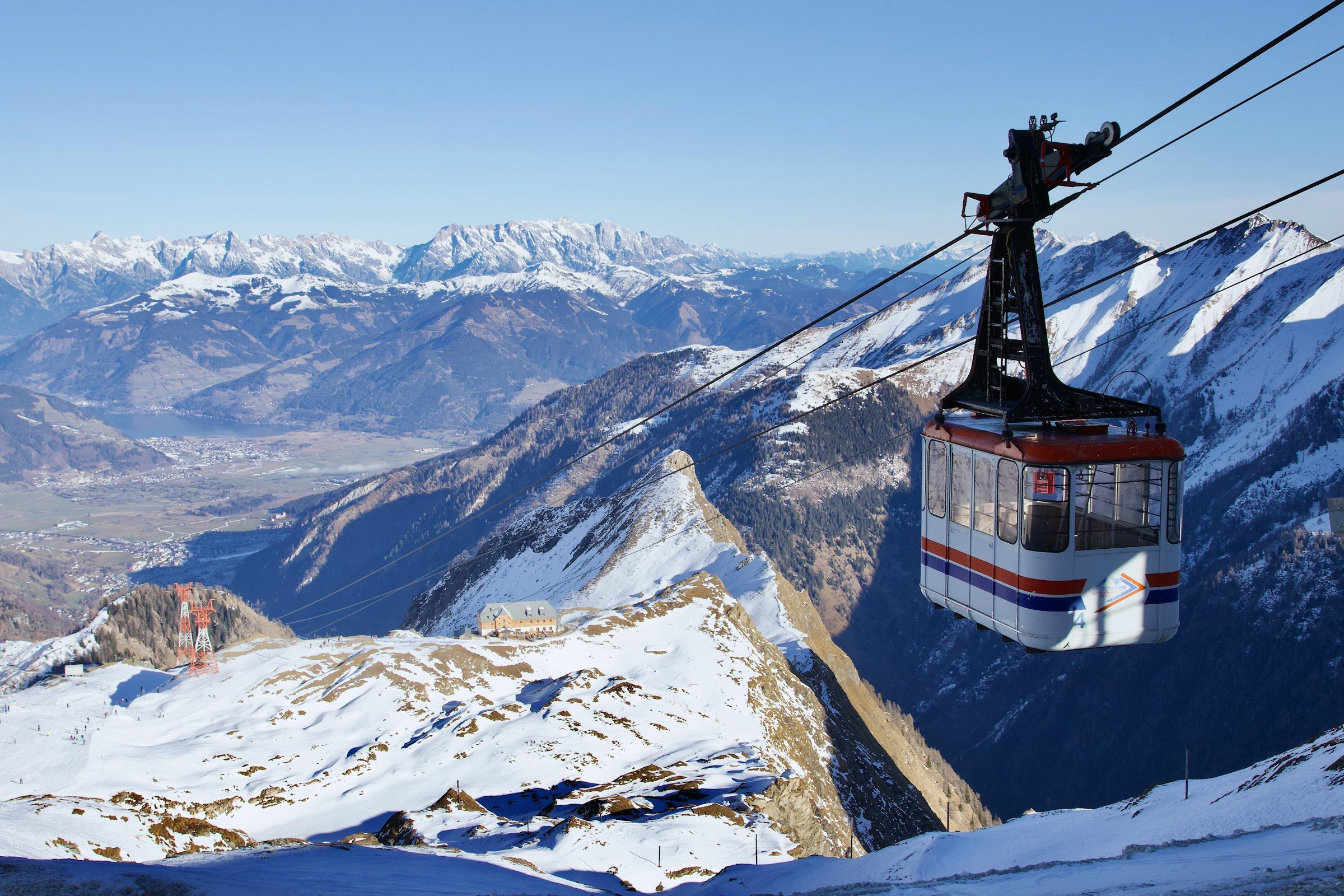 Skidlift åker nedåt för en skidbacke med mäktiga snötäckta berg i bakgrunden i Zell am See