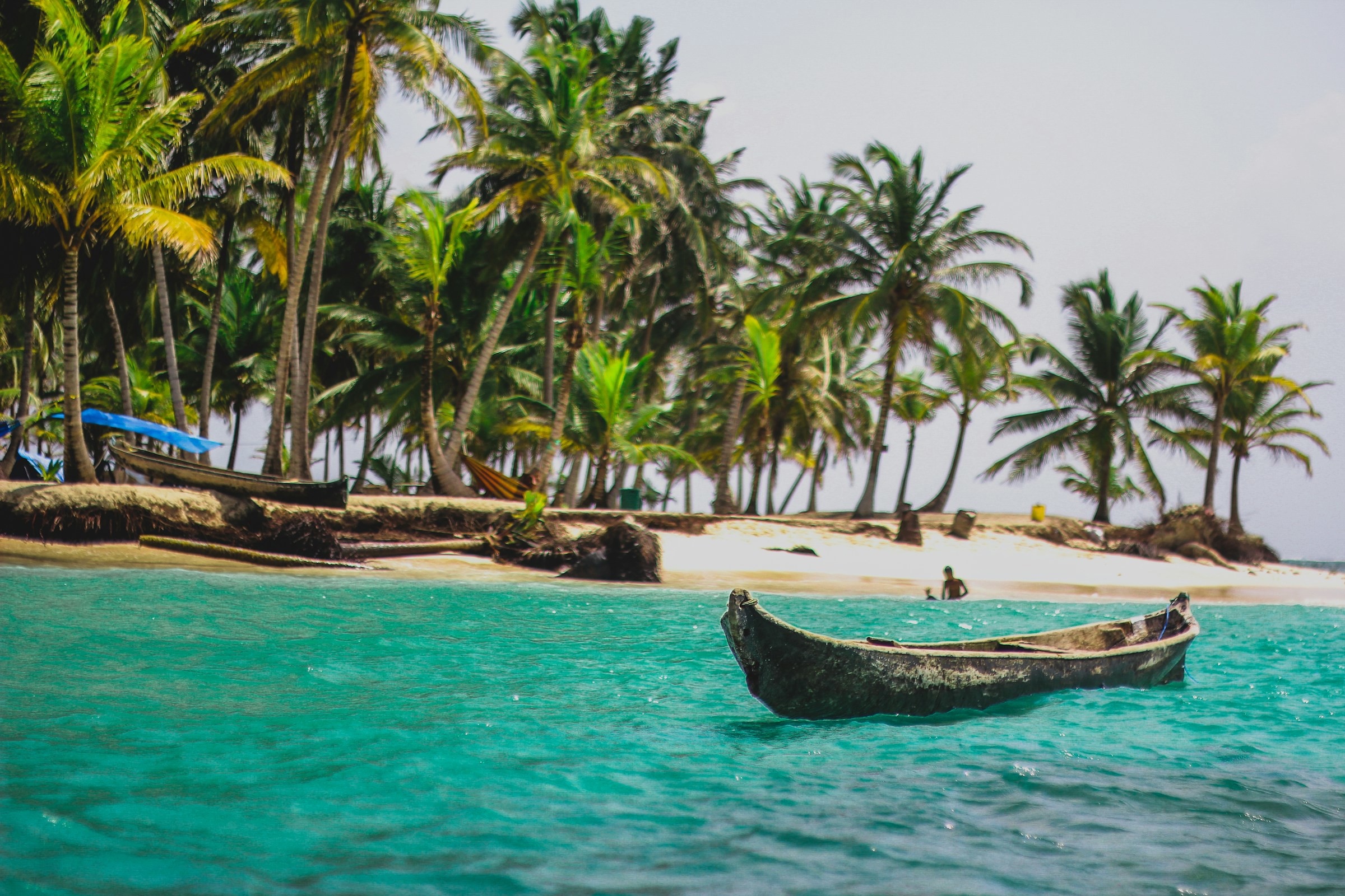 En mindre träbåt ligger i klarblått vatten vid en vacker strand med palmer i Panama