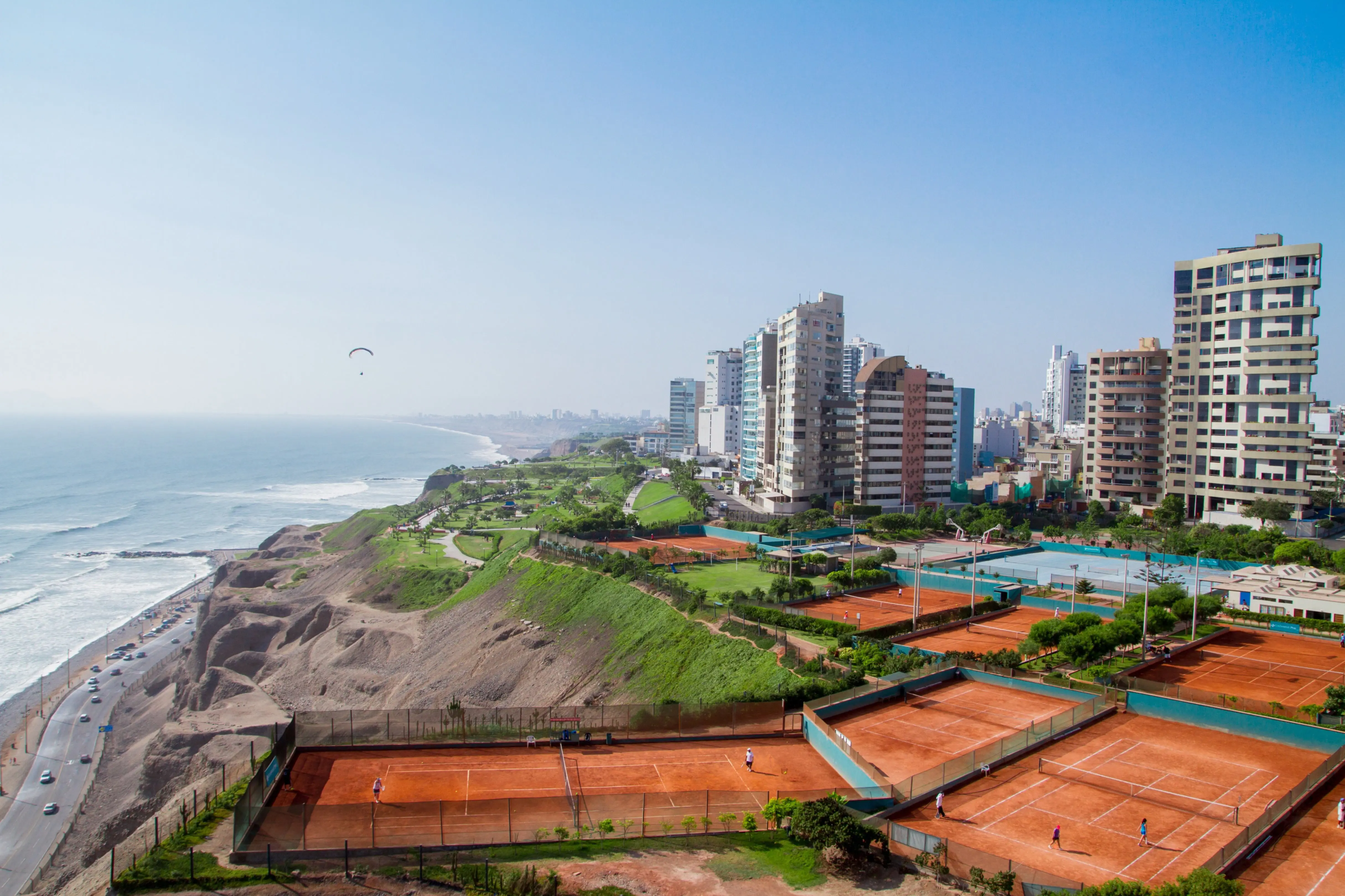 Resa till Lima - Vu över kusten där havet möter stadskanten av Lima i Peru med byggnder, tennisplan och blå himmel