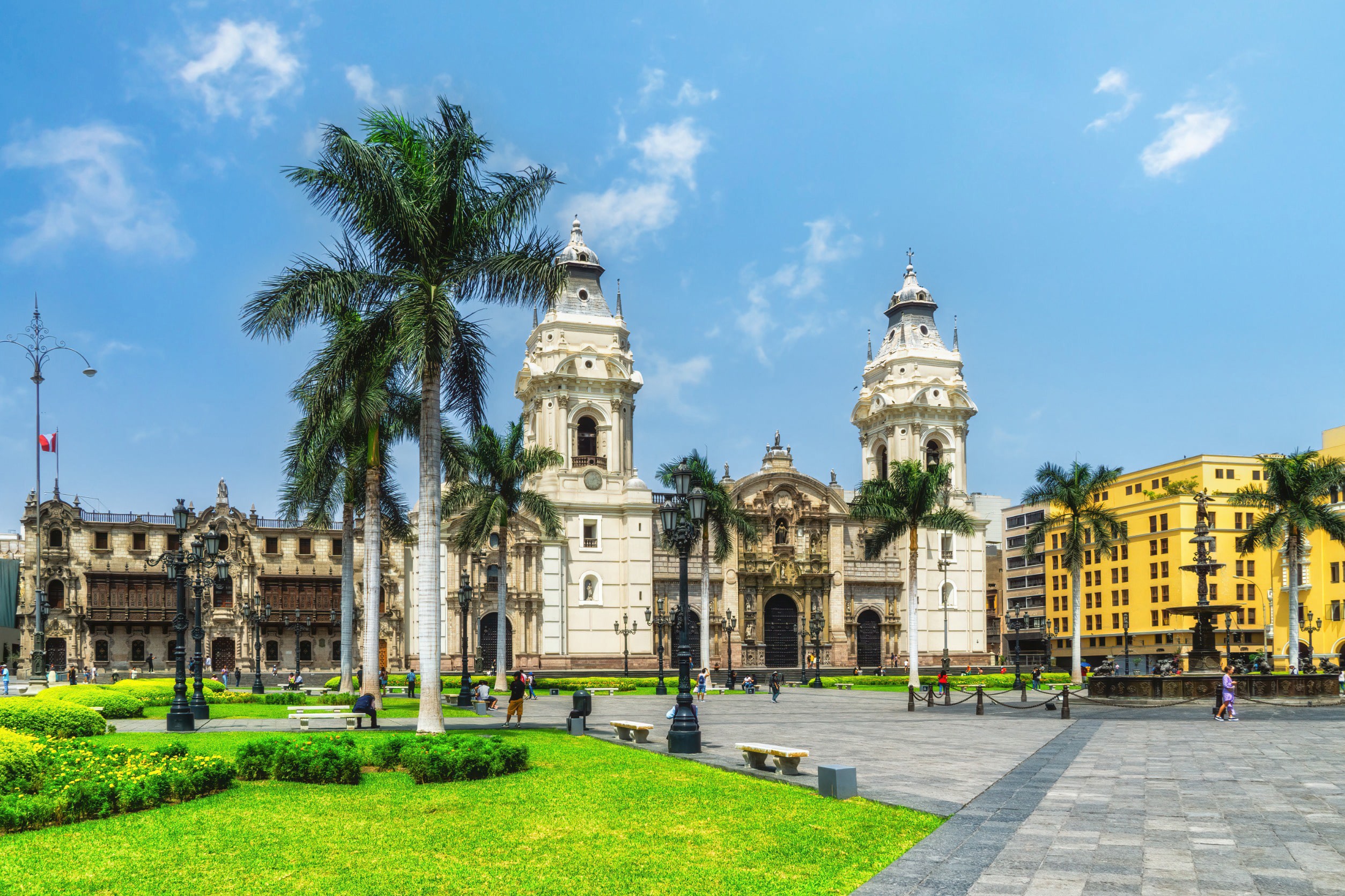 Vackert torg men grönt gräs, palmer och tradtionella spanska byggnder i vit och gult i Lima, Peru