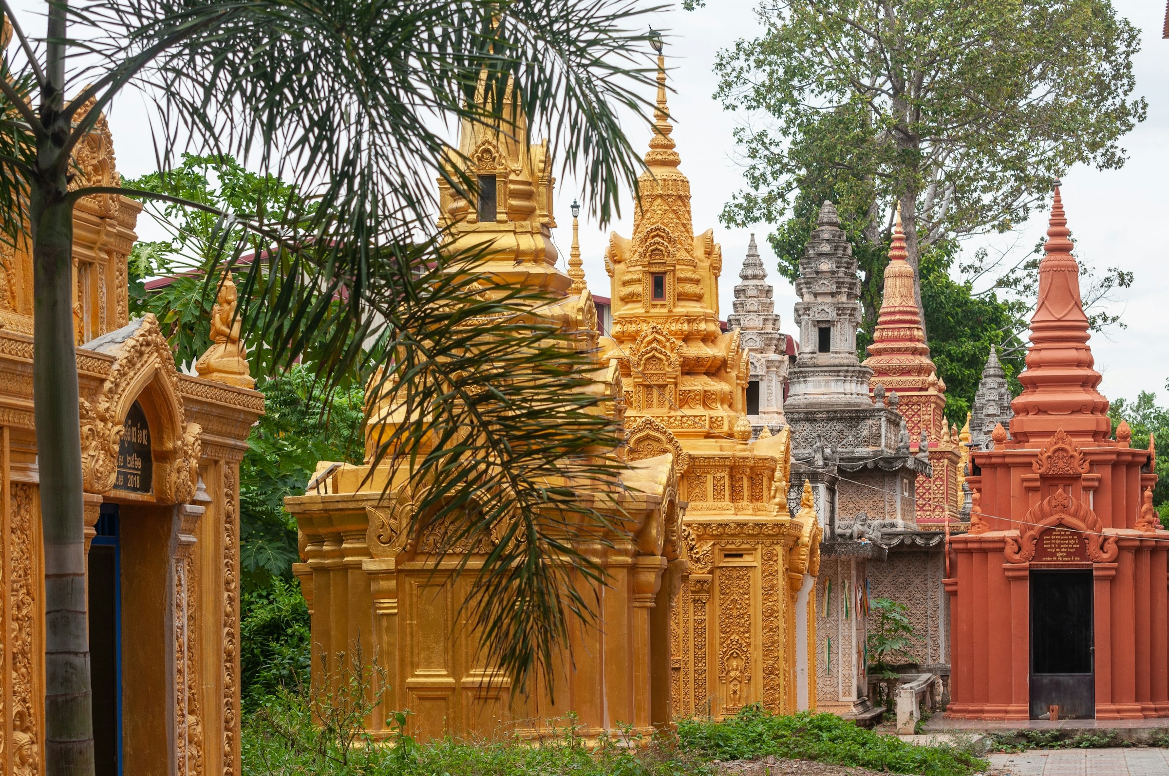 Traditional golden and terracotta stupas at a temple surrounded by greenery in Phnom Penh.