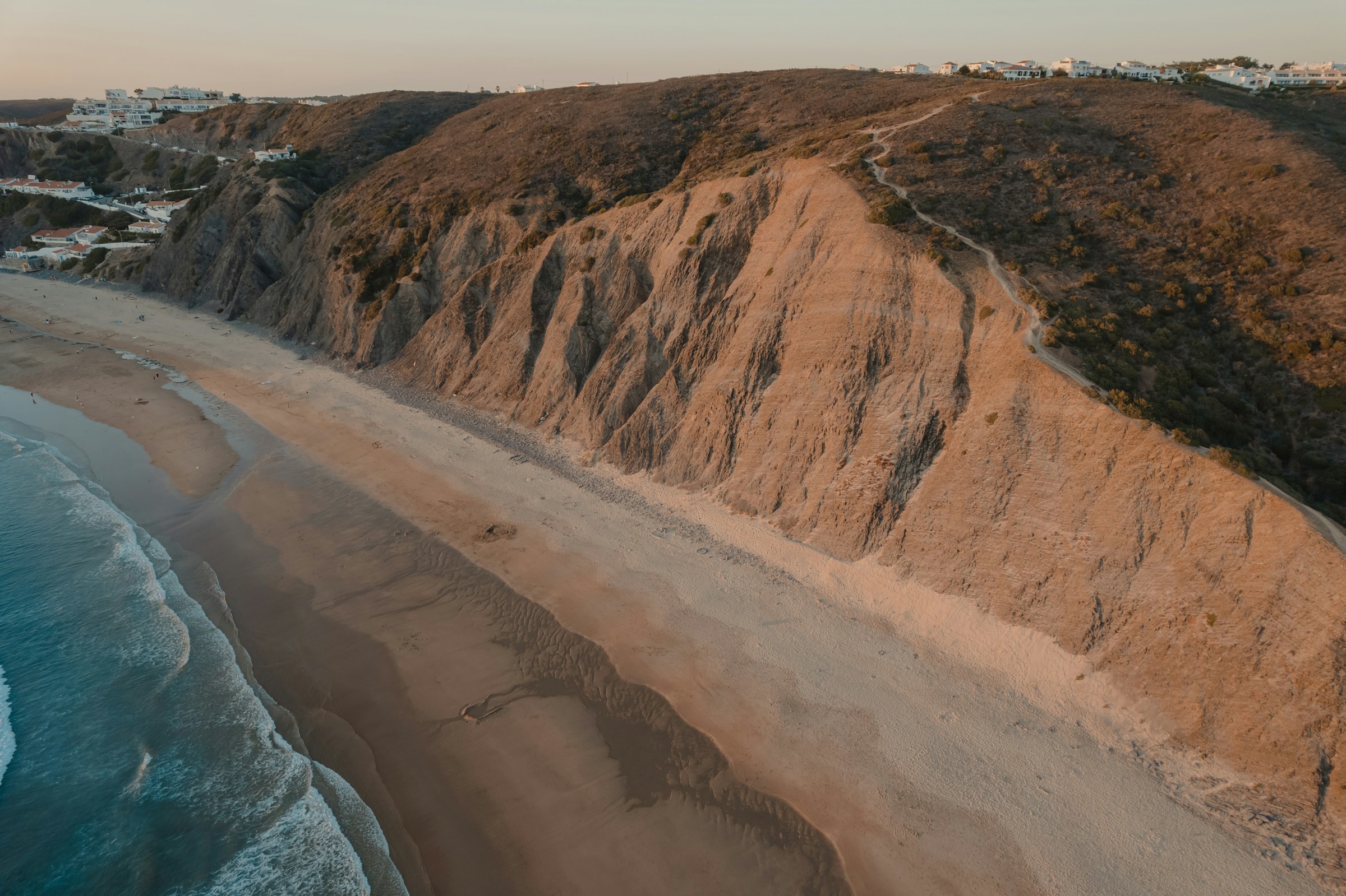 Lång vacker tom sandstrand med havet och stora klippor med en vit stad i bakgrunden i kanten av Algarve