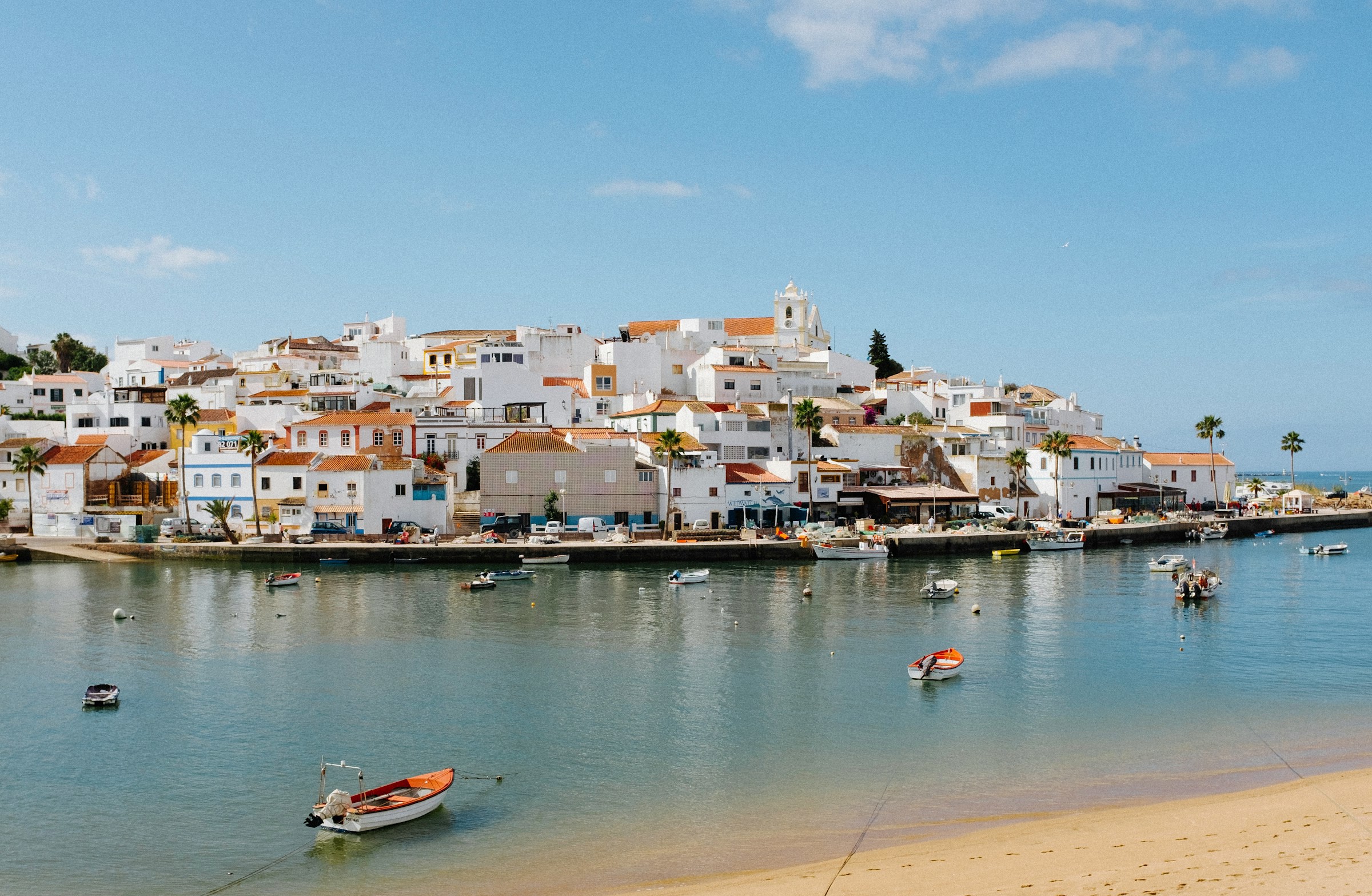 Blått vatten med småbåtar kring en liten hamn med vita byggnader i södra Portugal