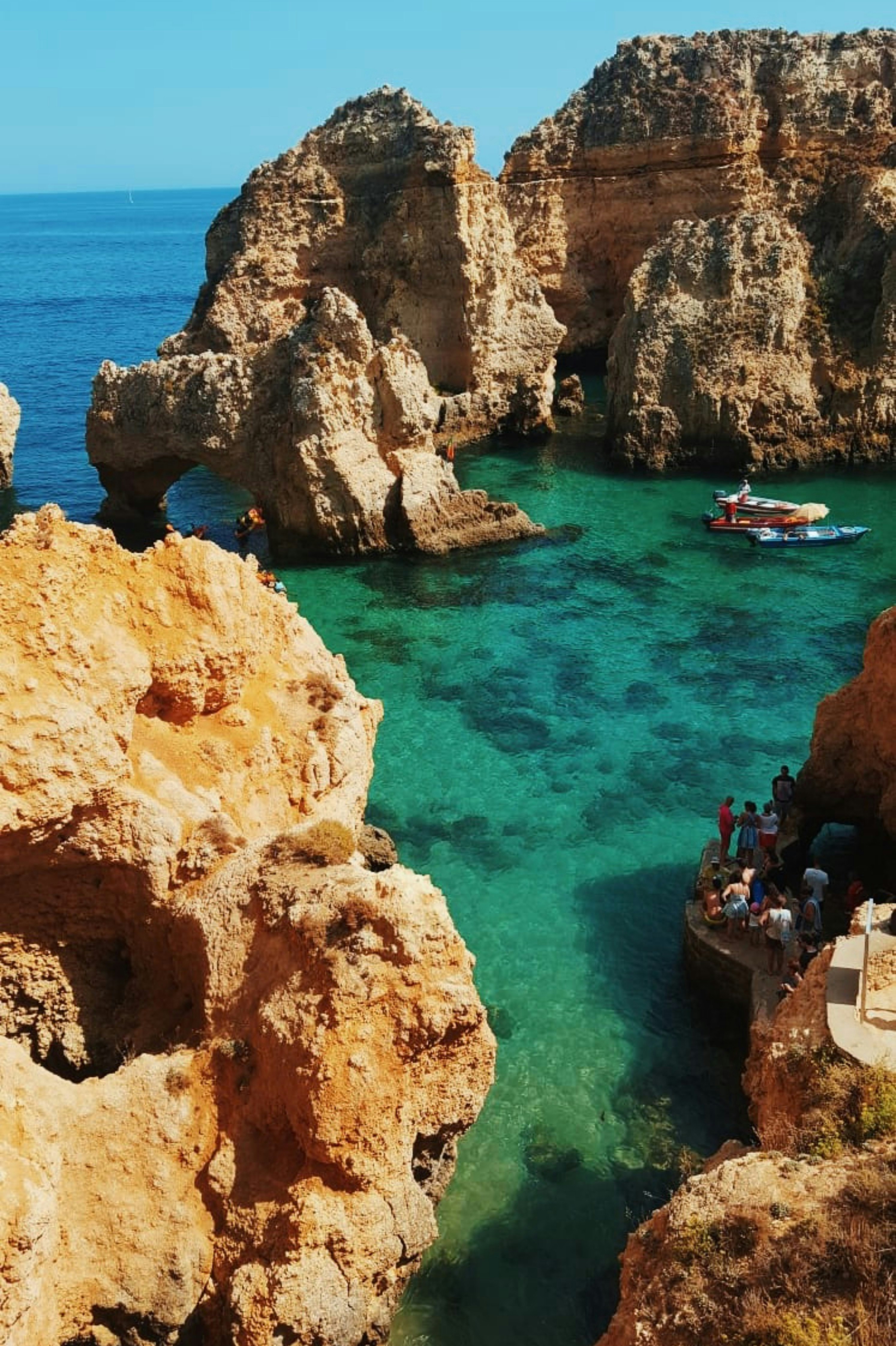 Klippor kring en bukt med turkosblått hav och en båt i Algarve, Portugal