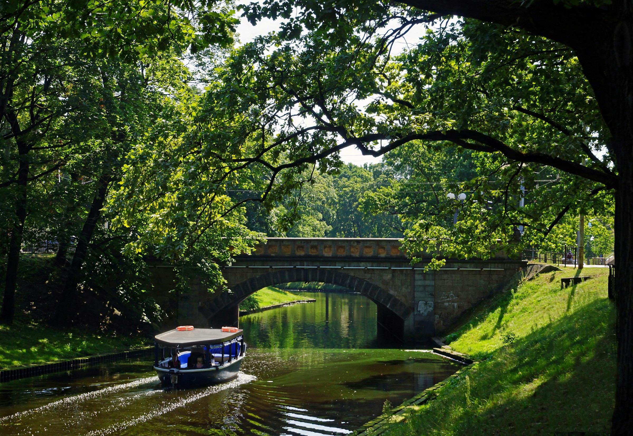 En kanal genom grönskande skog med en liten båt i centrala Riga, Lettland en solig sommardag.