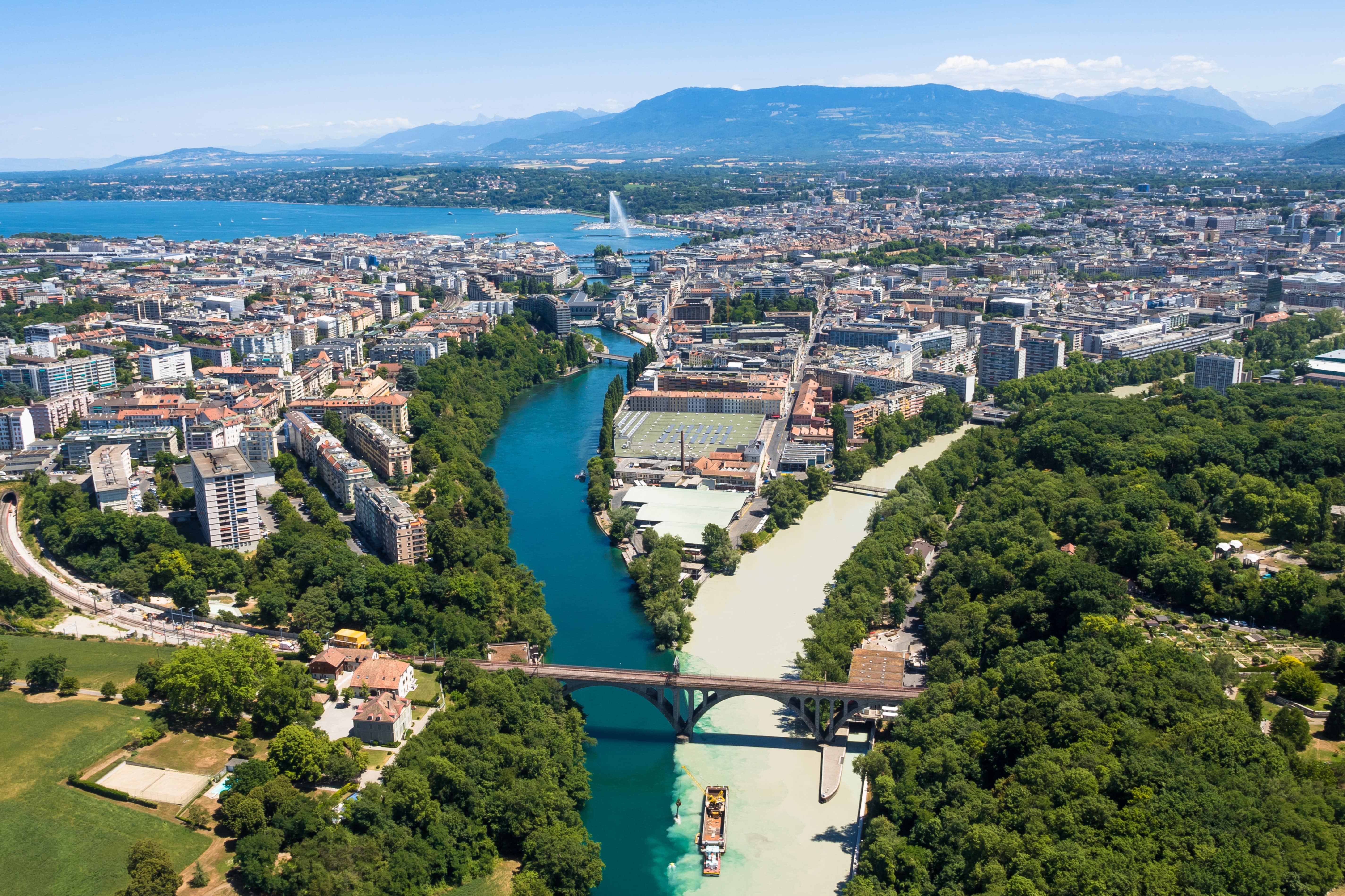 Travel to Geneva - View from above of Geneva city with greenery and a blue river running through the city and mountains in the background