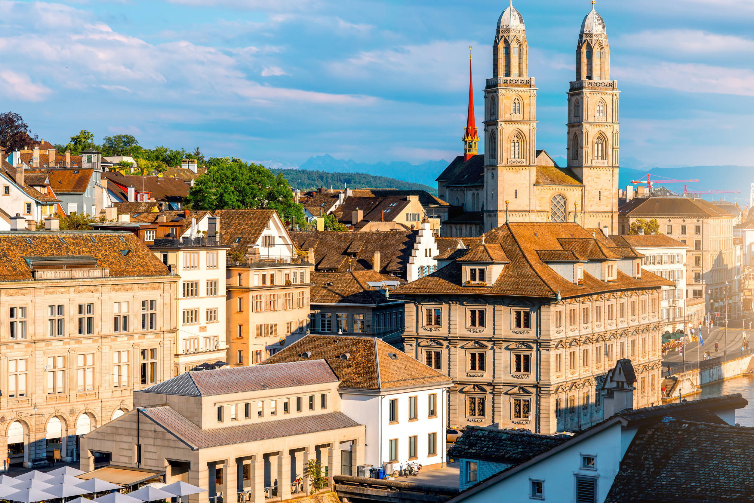 Vacker kyrka med två torn bland äldre byggnader i Zurich med blå himmel i bakgrunden