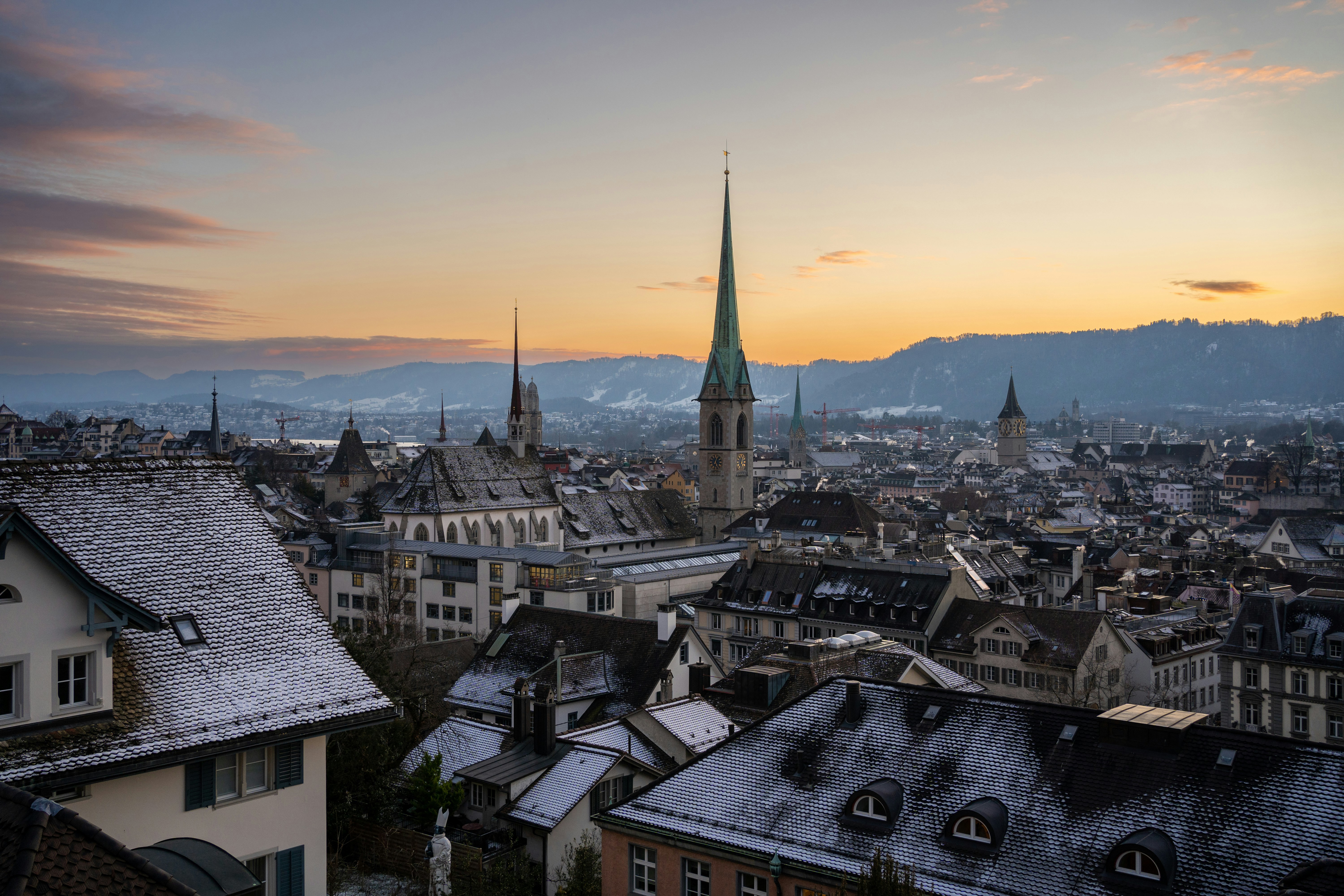 Solnedgång över Zürich-stad under vintertid men snötäckta hustak och ett kyrkotorn i bakgrunden