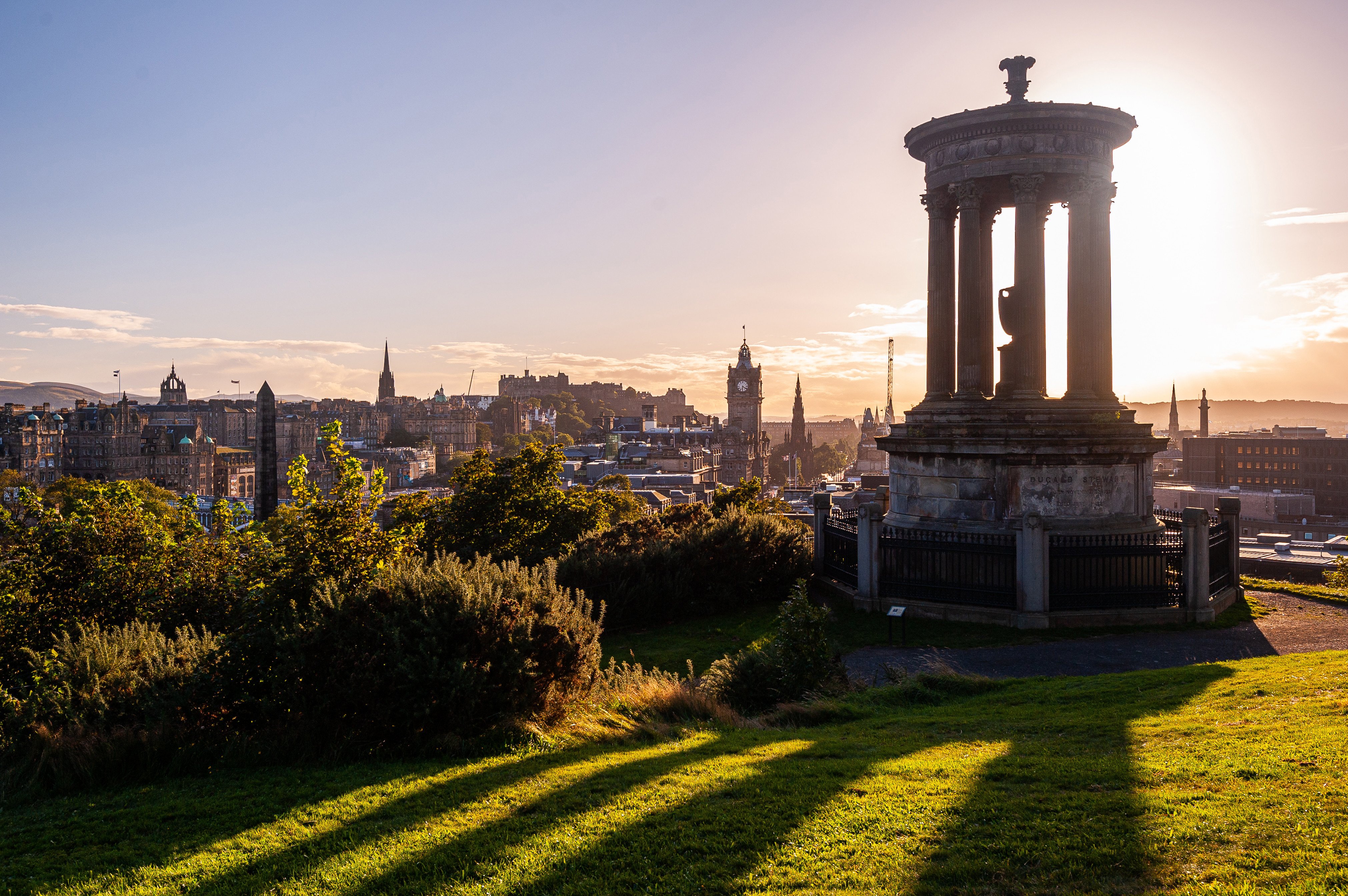 Solnedgång vid en skulptur på en kulle över Edinburgh med stadsmiljö i bakgrunden