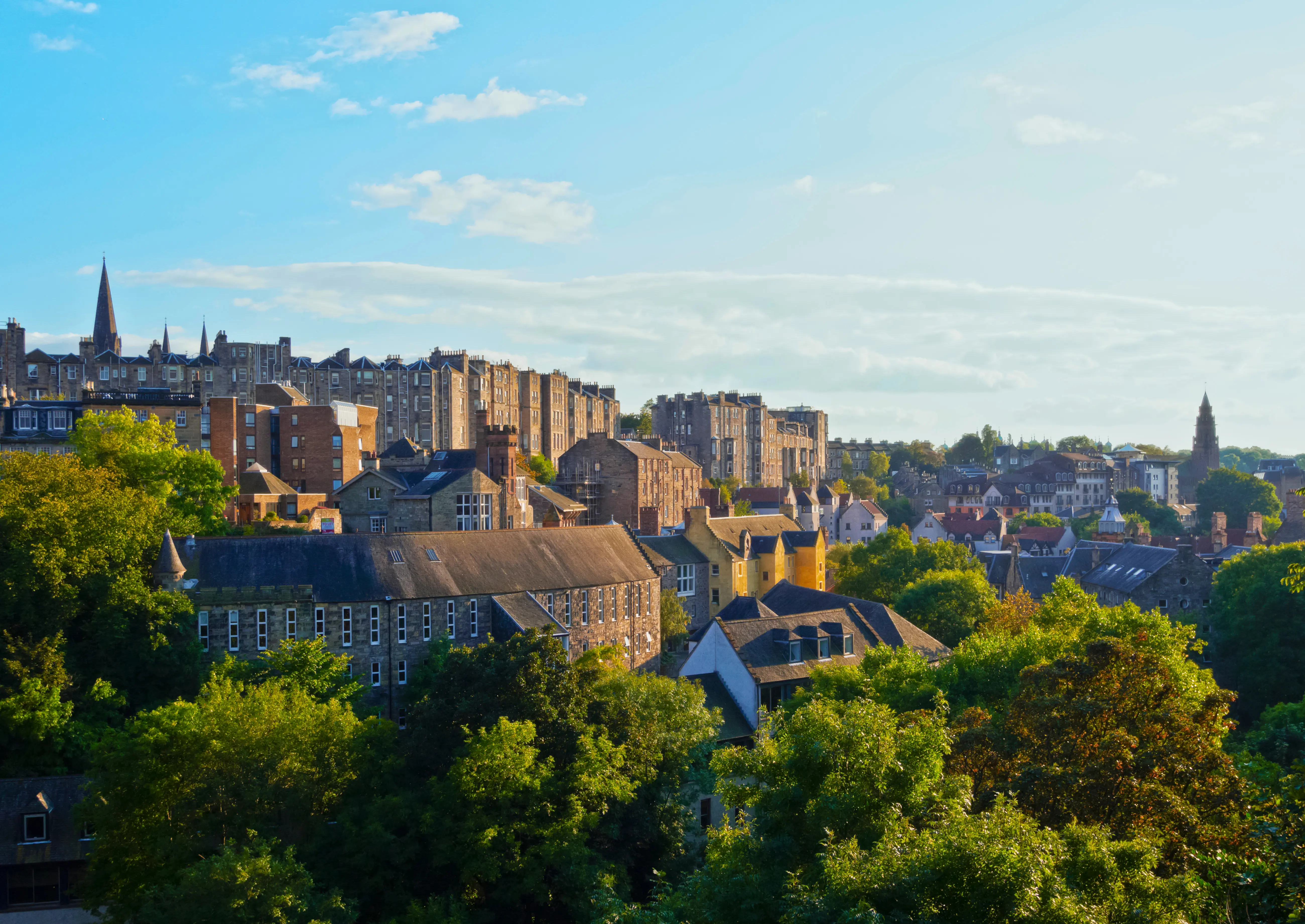 Resa till Edinburgh - Panoramautsikt över historiska stenhus och gröna träd i en stad vid solnedgång.