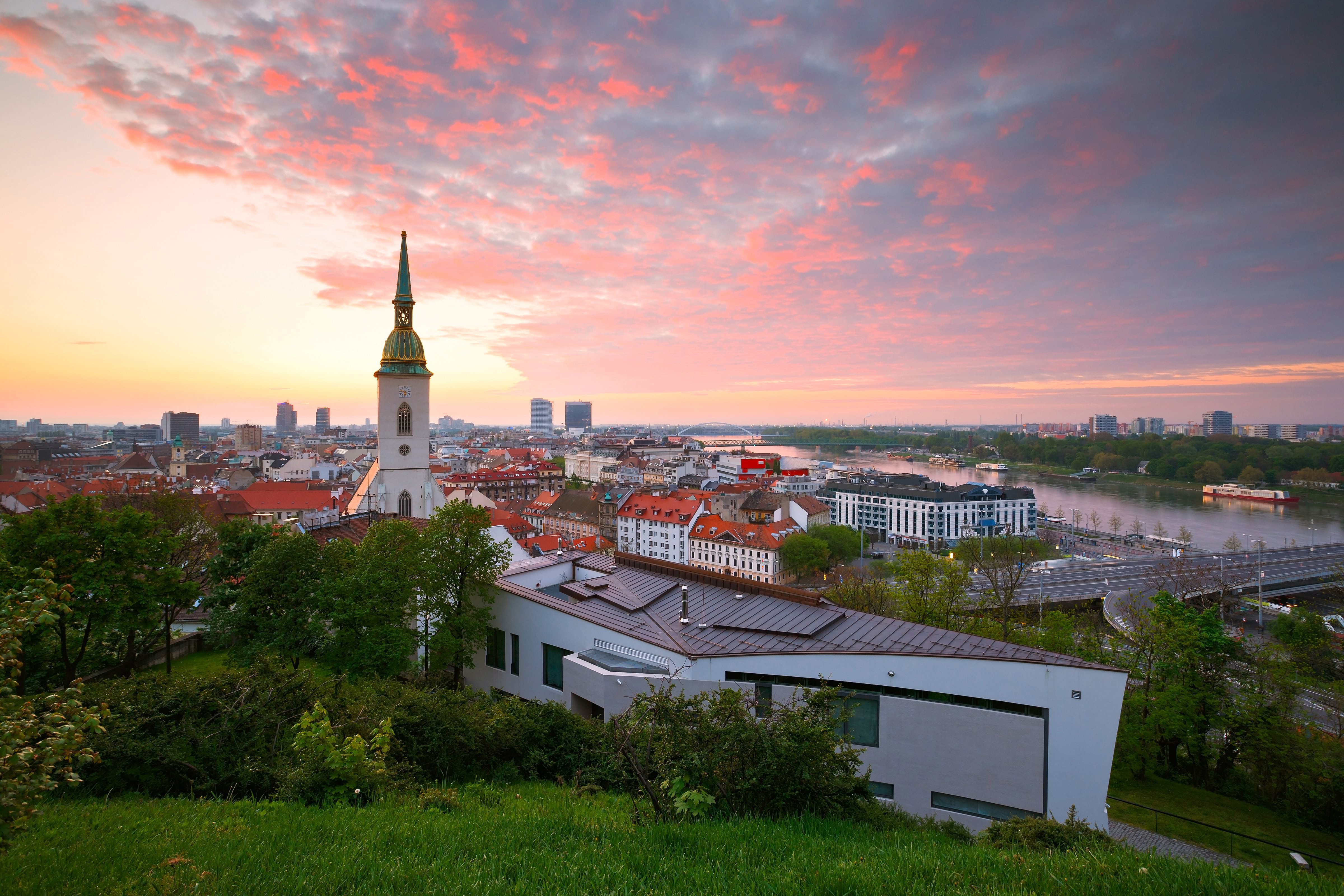 Solnedgång över Bratislava med ett vackert kyrktorn som sticker upp mot en rosa himmel