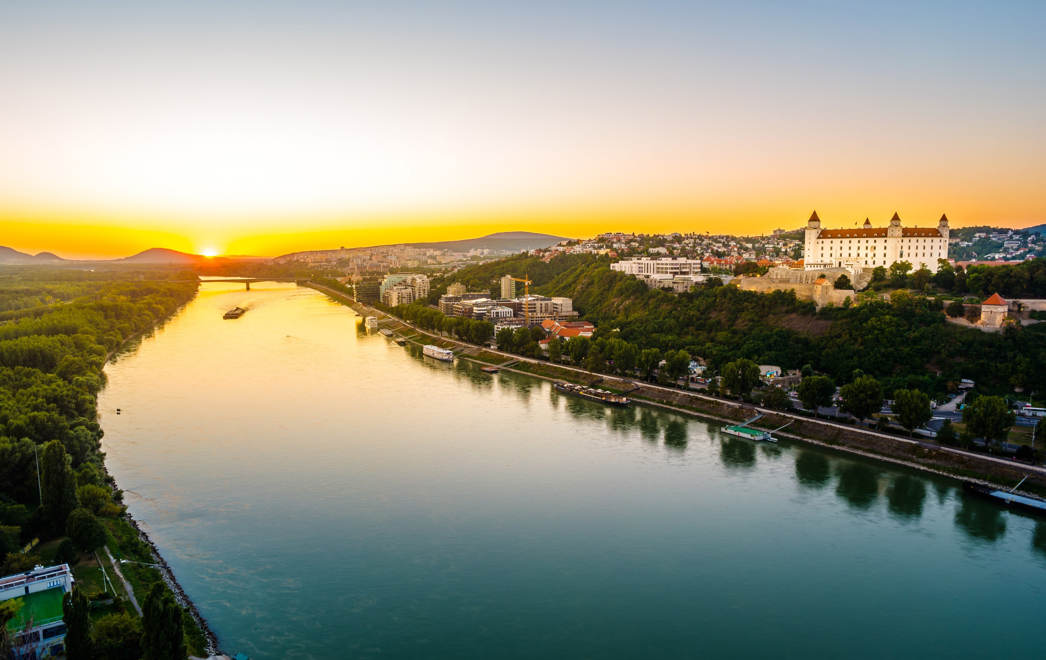 Solnedgång över en flod som löper genom Bratislava med staden i bakgrunden