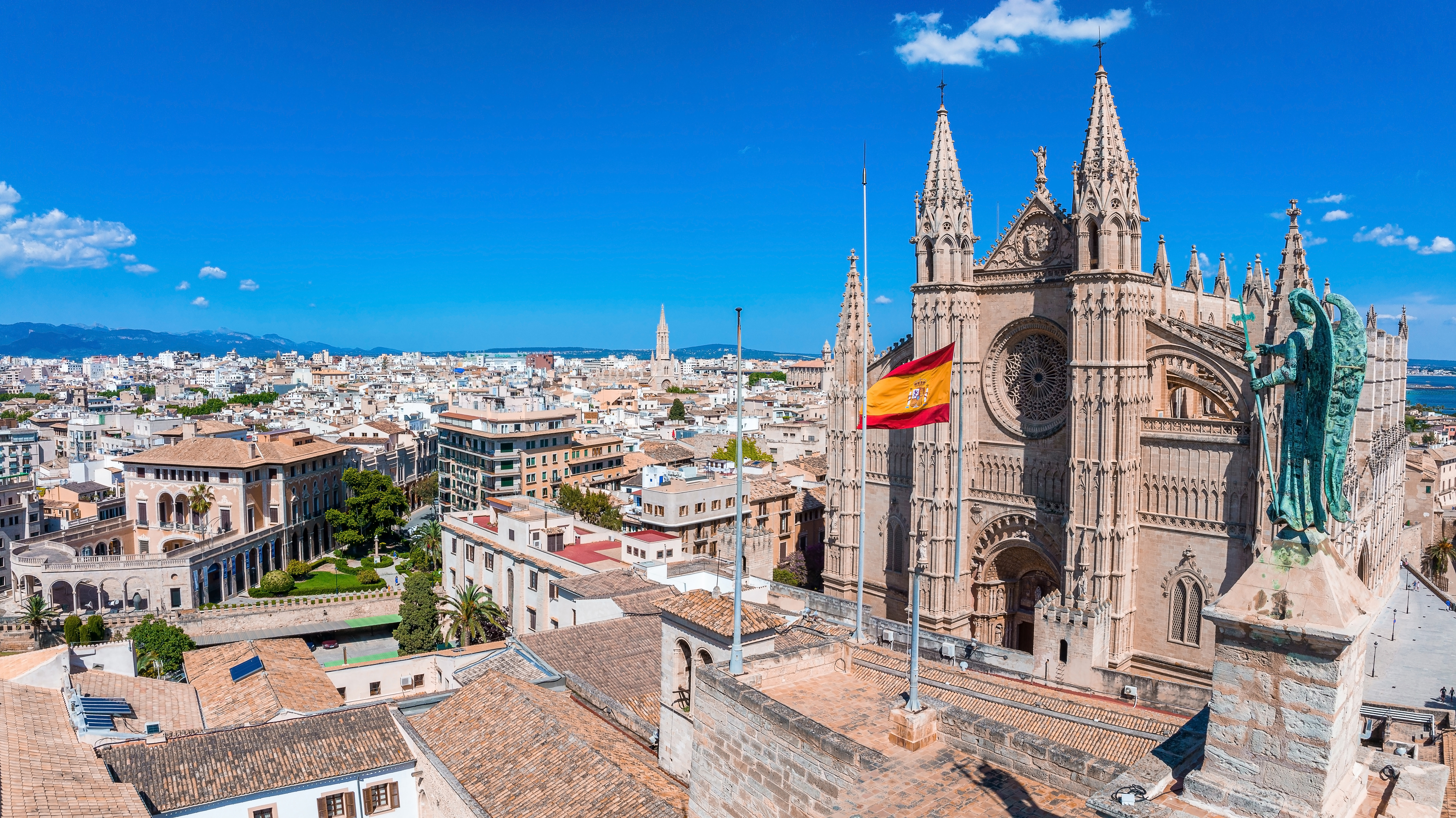 anoramavy över Palma de Mallorcas stadssilhuett i Spanien, med katedralen La Seu i förgrunden och den spanska flaggan som vajar, klarblå himmel.