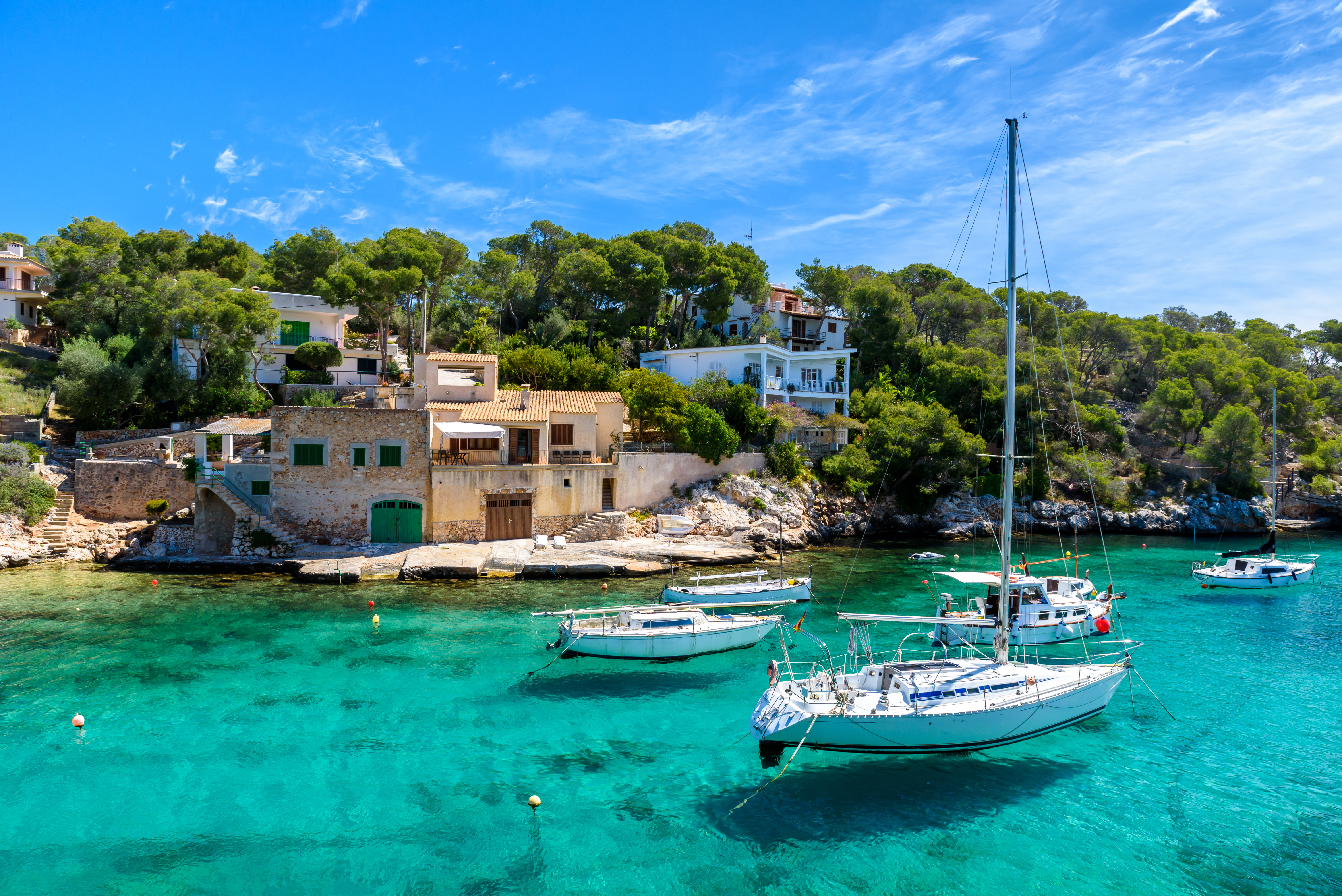 Resa till Mallorca - Idyllisk utsikt över en klarblå vik med segelbåtar och medelhavsstil hus på Mallorca