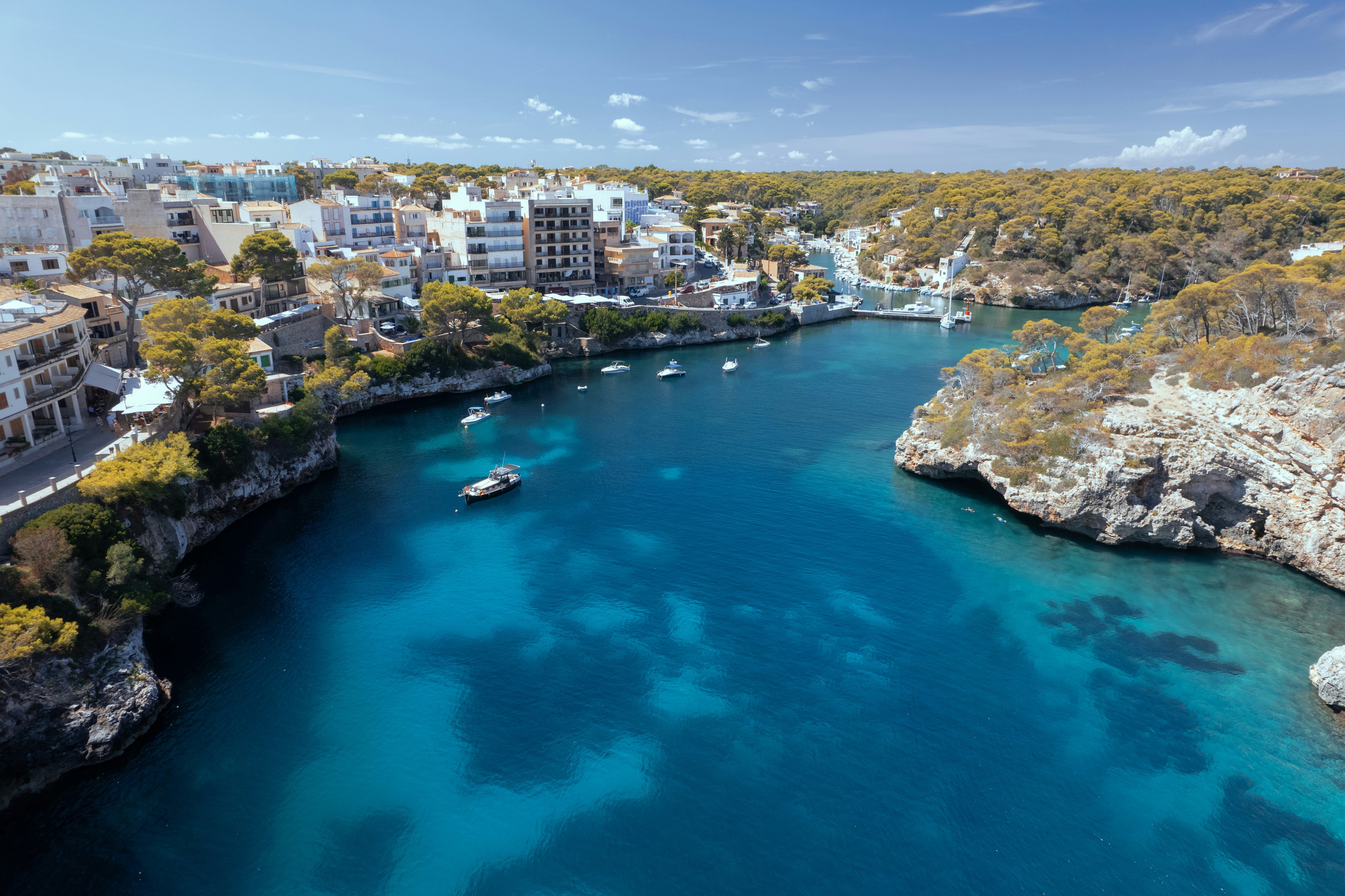 Luftbild av kuststad med kristallklart vatten och båtar i en vik på en solig dag på Mallorca