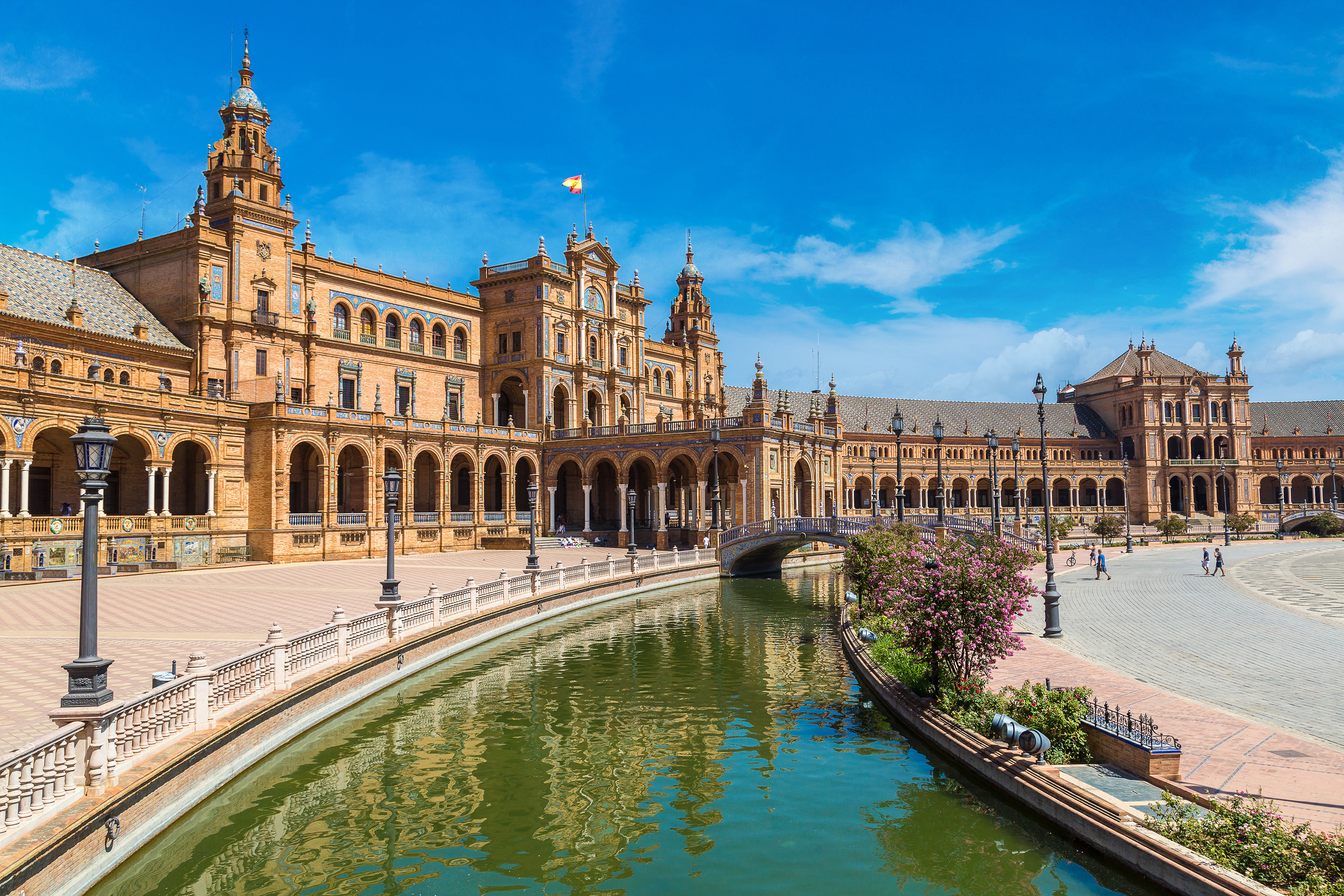 Resa till Sevilla - Plaza de España i Sevilla med arkadgångar, fontäner och kanal under en klarblå himmel.