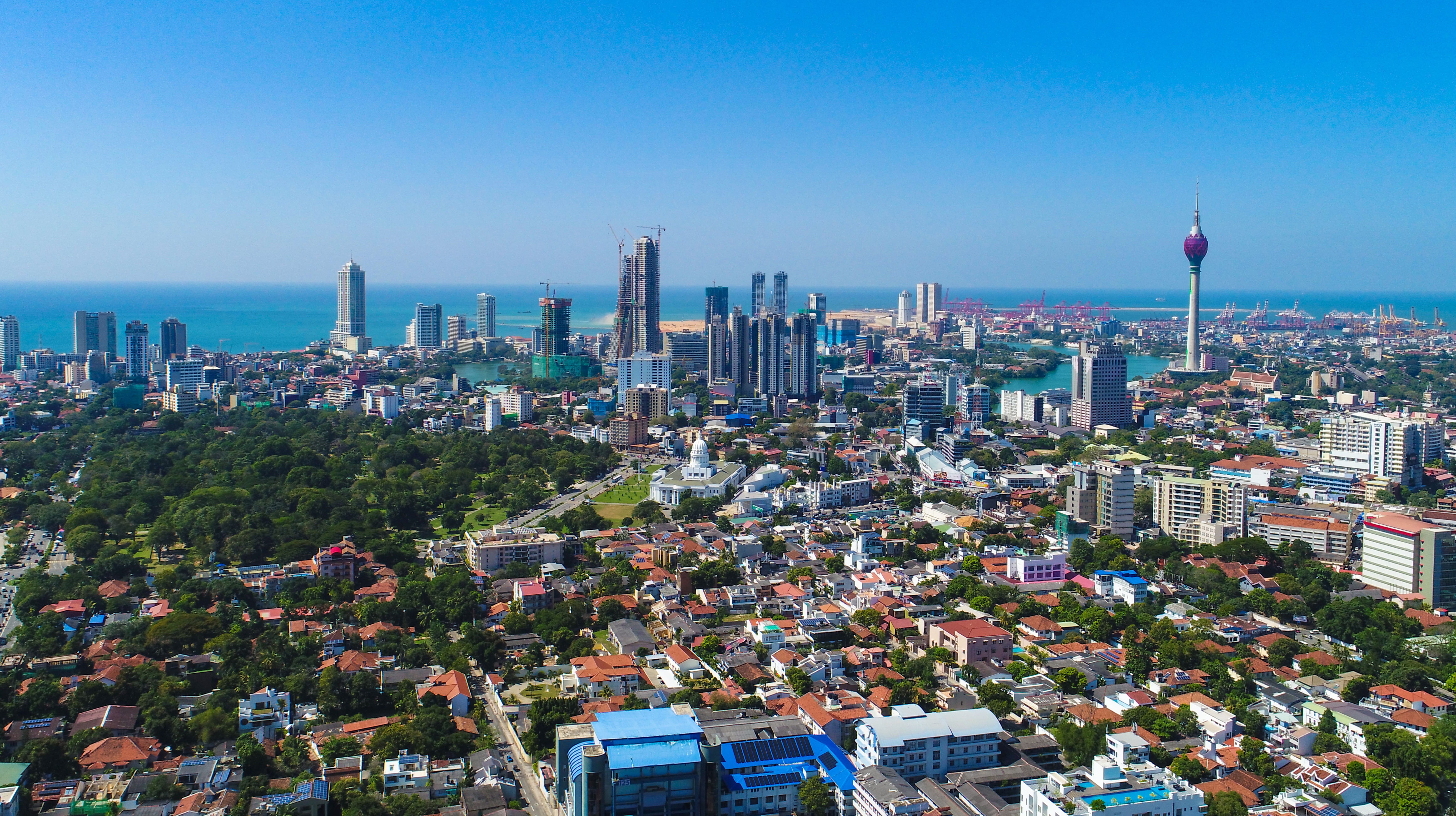 Travel to Colombo - Panoramic view of city with greenery and buildings meeting a coast of blue sea and blue sky