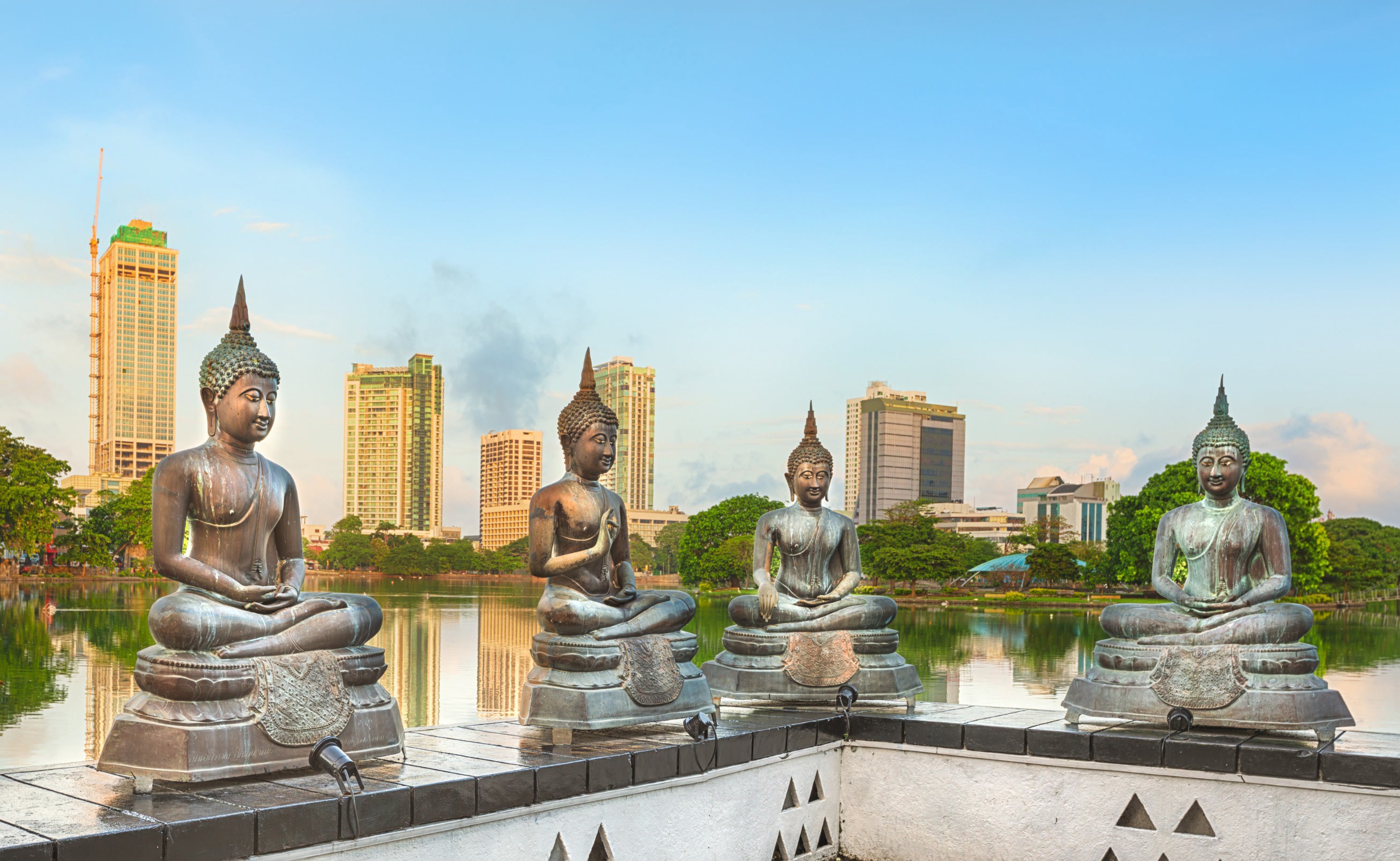 Religious statues with green trees around them and skyscrapers from Colombo city in the background