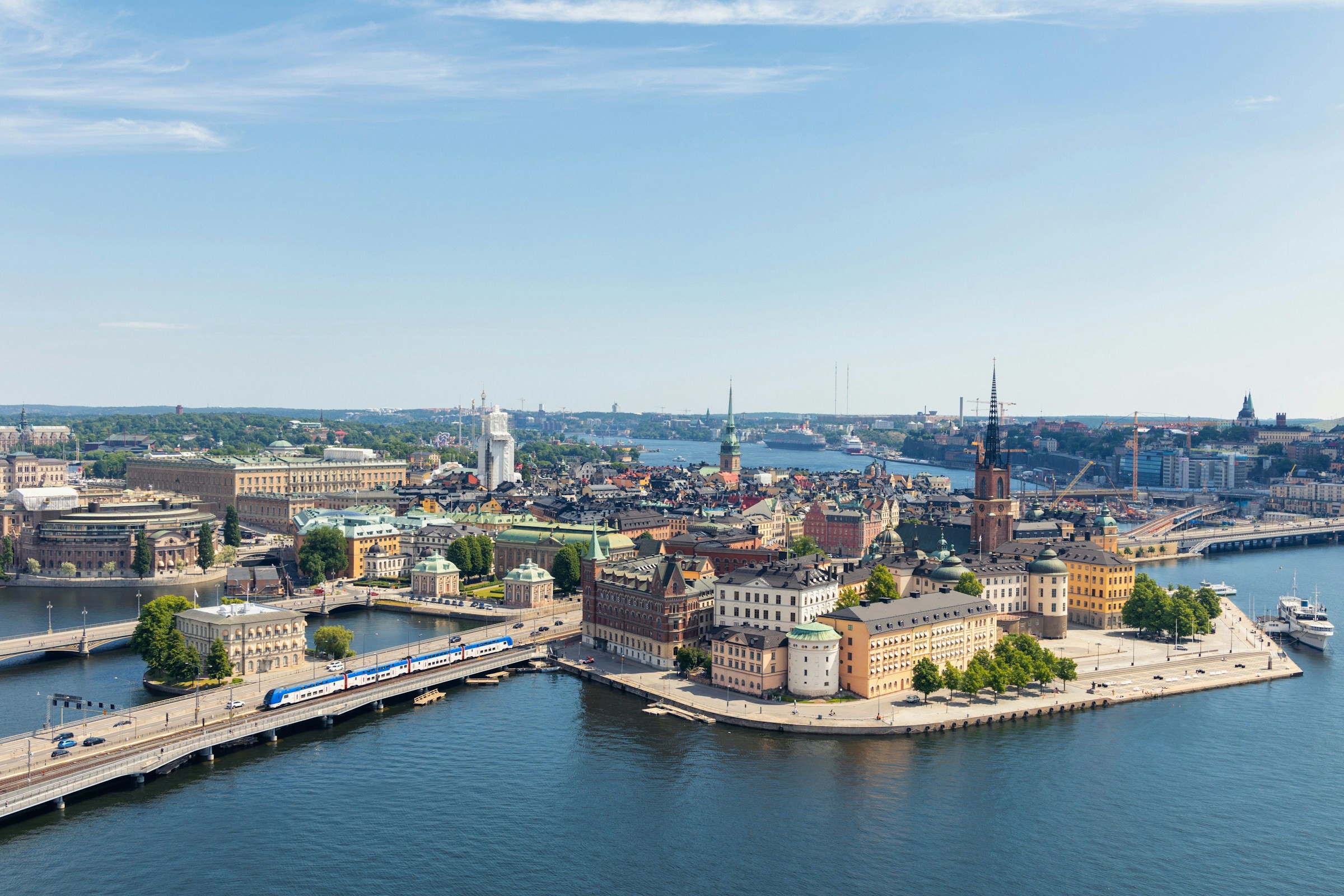 Panoramavy över Stockholm med Gamla Stan och Strömmen, synliga broar och historiska byggnader under en klarblå himmel.