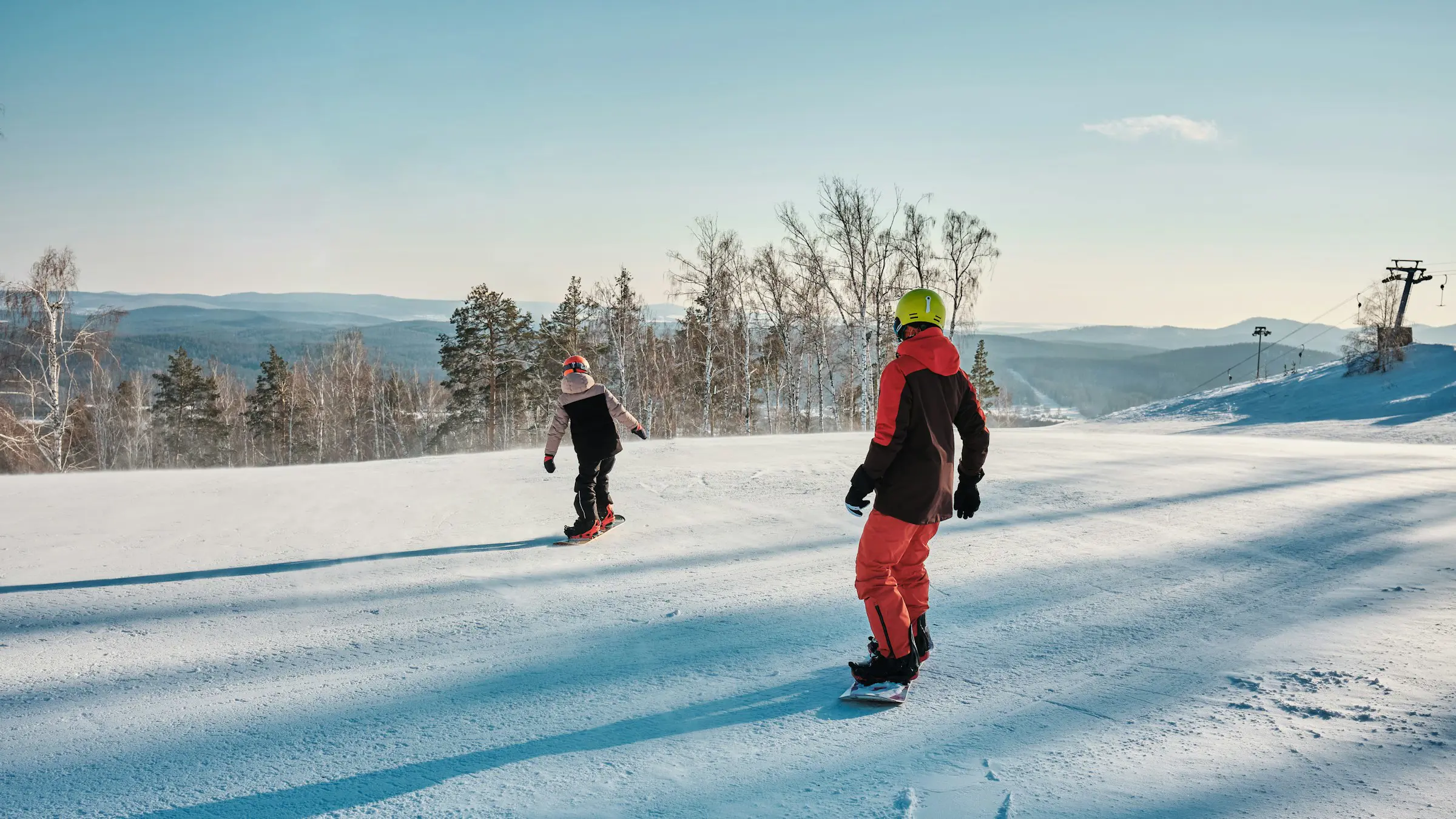 Resa till Sälen - Två personer åker snowboard ner för en snötäckt backe med utsikt över träd och berg