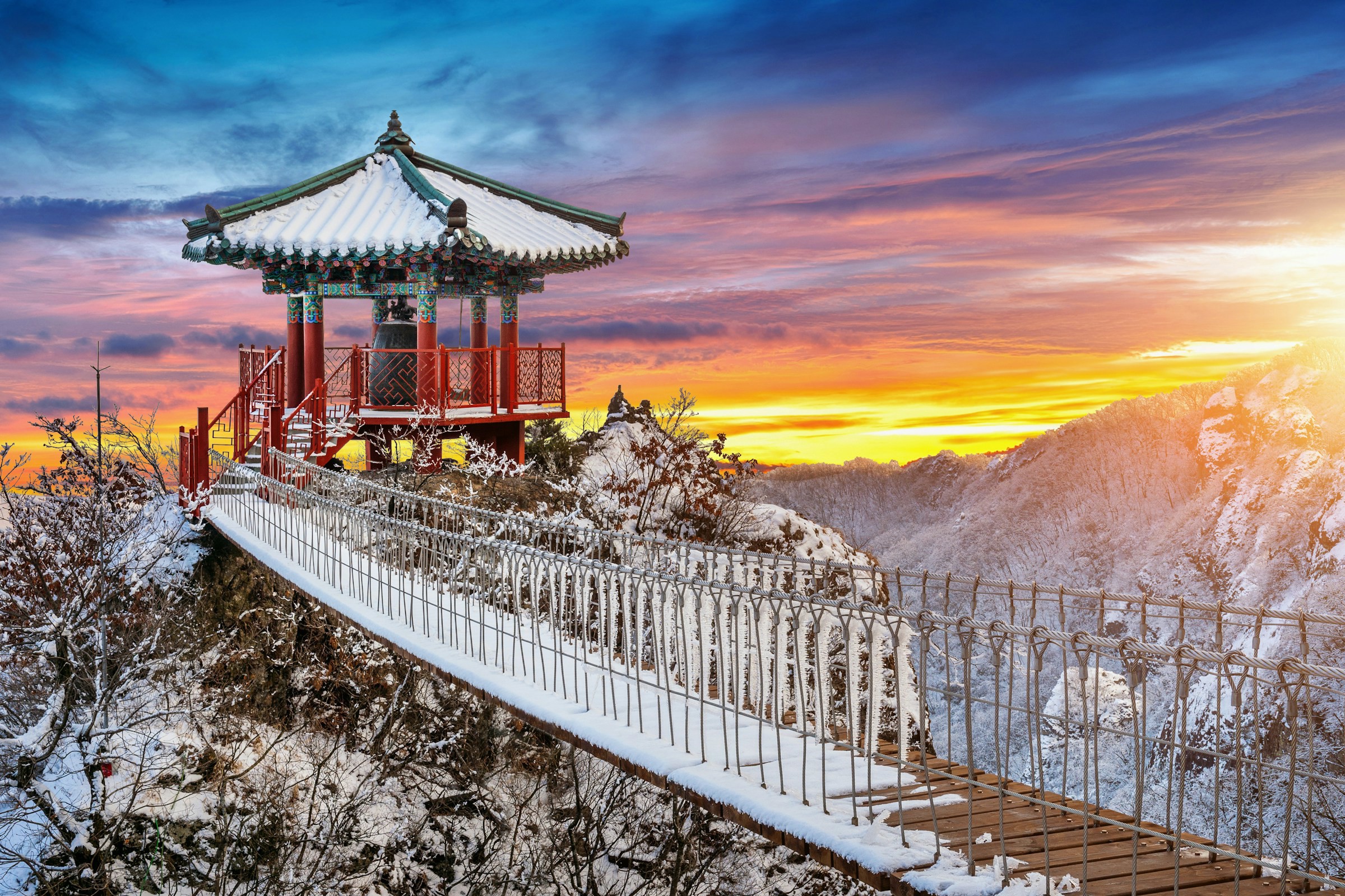 En snötäckt bro går över till ett sydkoreansk byggnad blad bergen under en vacker solnedgång