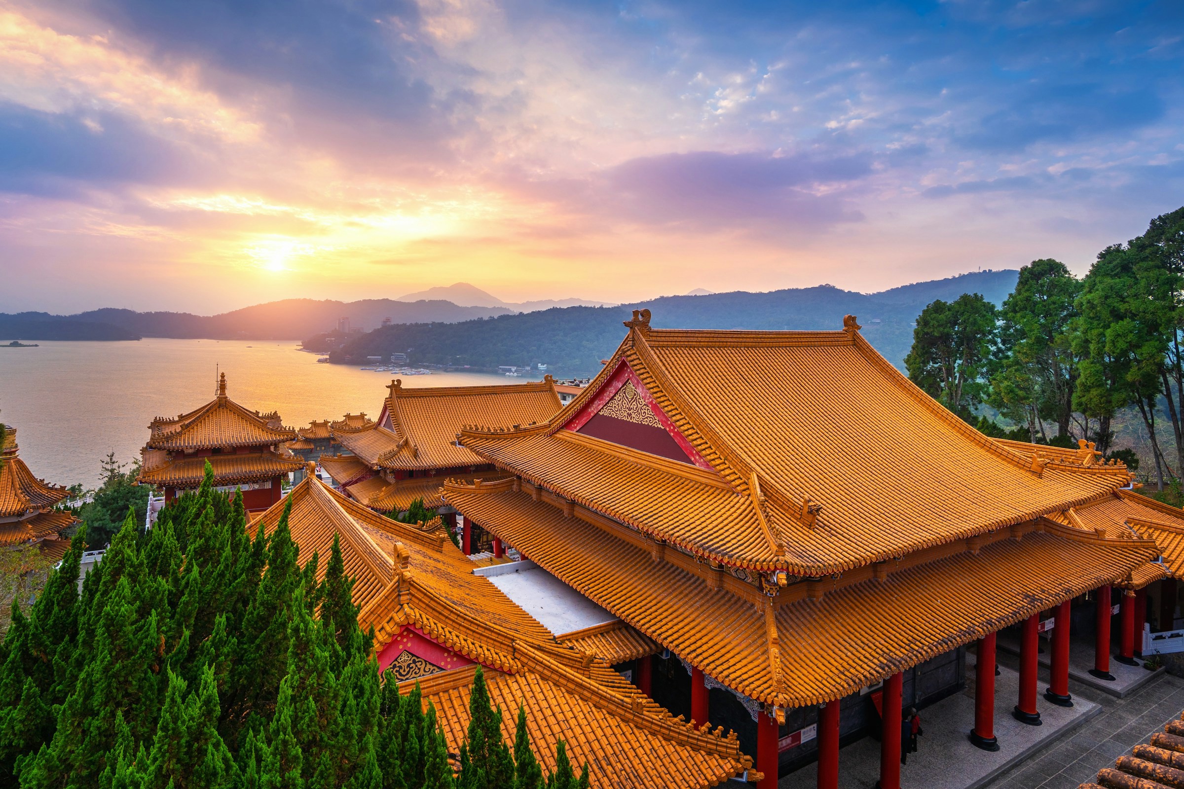 Tempel i Taiwan med gult tak och djungel runtomkrign sig möter havet under en solnedgång